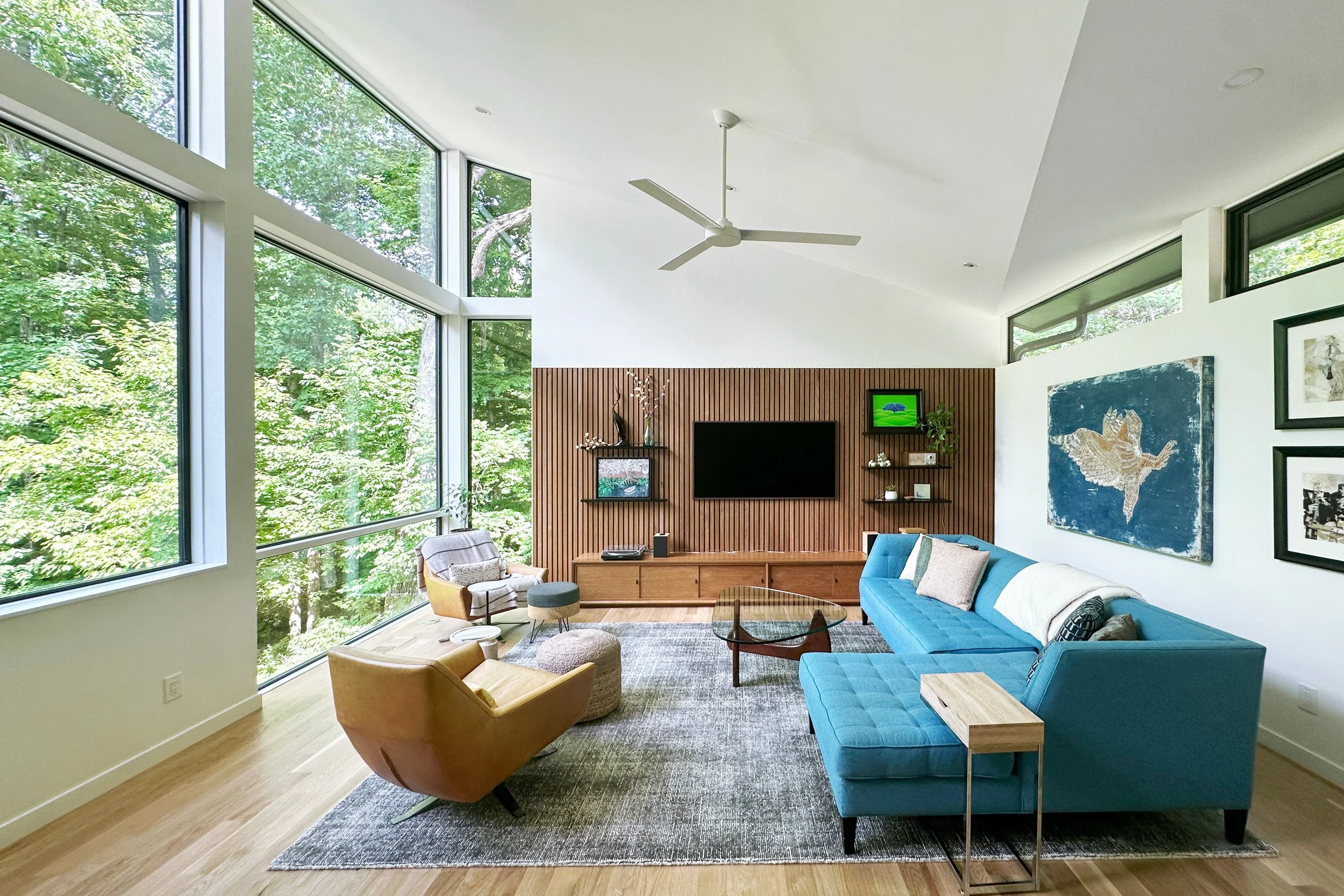  The roof tilts up to the dramatic view in the living room, with large windows following the ceiling plane. A custom built-in credenza and slatted acoustic wall echoes the vertical slats of the foyer. 