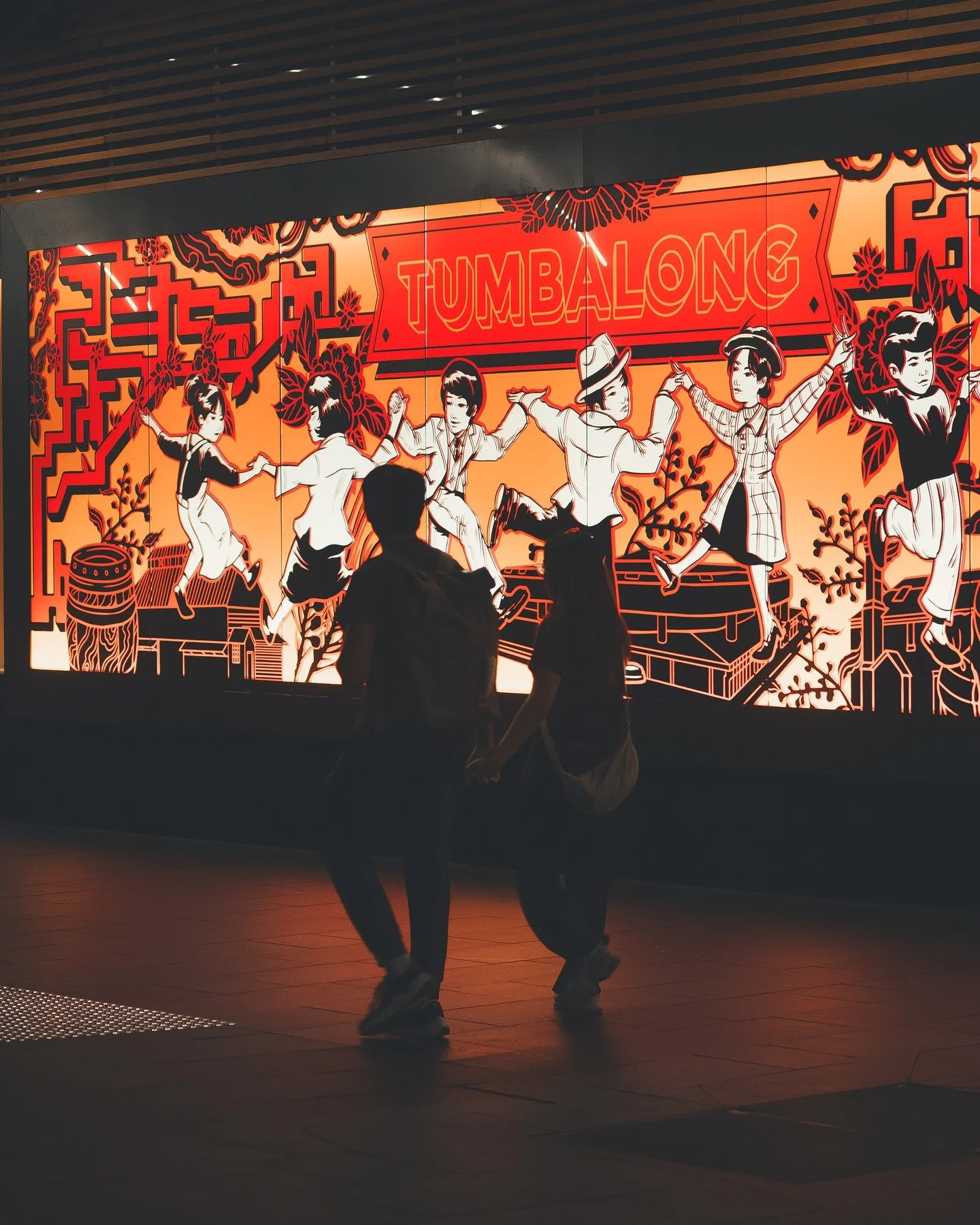 Faceless Sydney Pt:2 &ndash; It starts with movement&mdash;two silhouettes caught mid-step in front of the Tumbalong mural, where bold reds and playful lines celebrate joy, culture, and connection. A fleeting moment, unposed, yet perfectly placed.

T