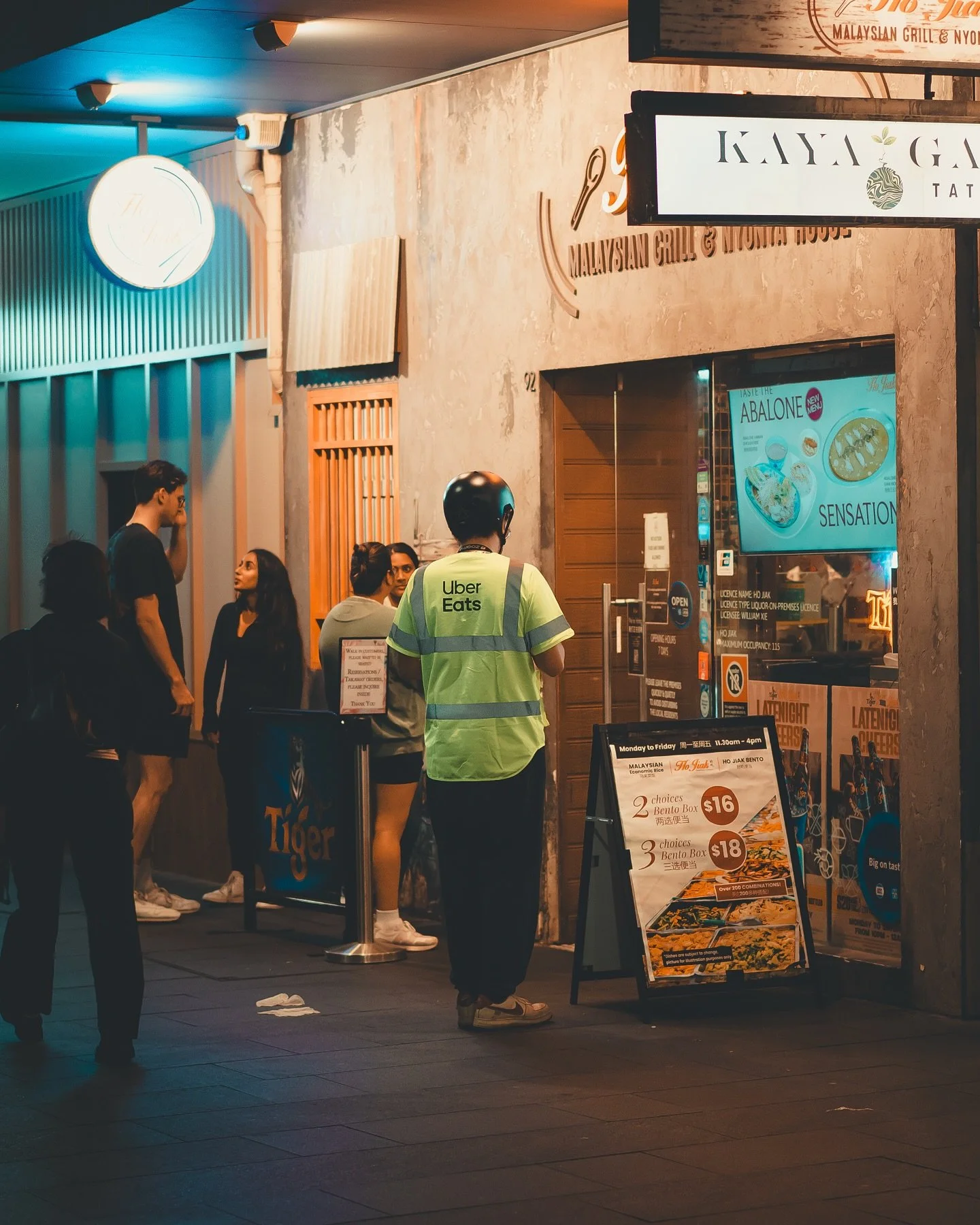 Faceless Sydney Pt:3 &ndash; Under the soft buzz of streetlights, the city settles into its evening rhythm. Conversations blend with footsteps, and the scent of dinner drifts through the air as the Uber Eats rider stands still&mdash;waiting, observin