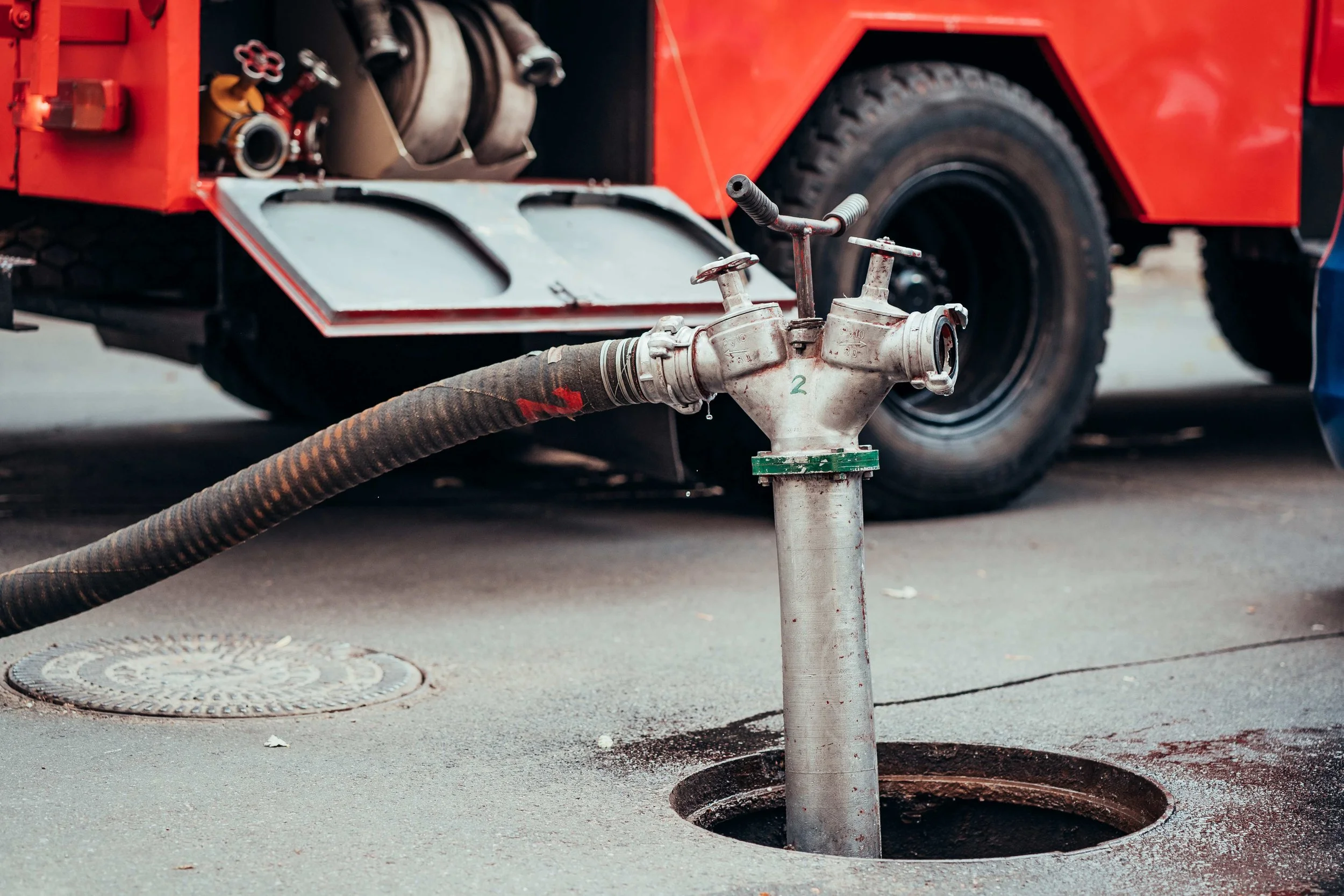 A fire truck with a red body, hose connections, and firefighting equipment parked on the street, with a dry hydrant hose connected to a fire hydrant.