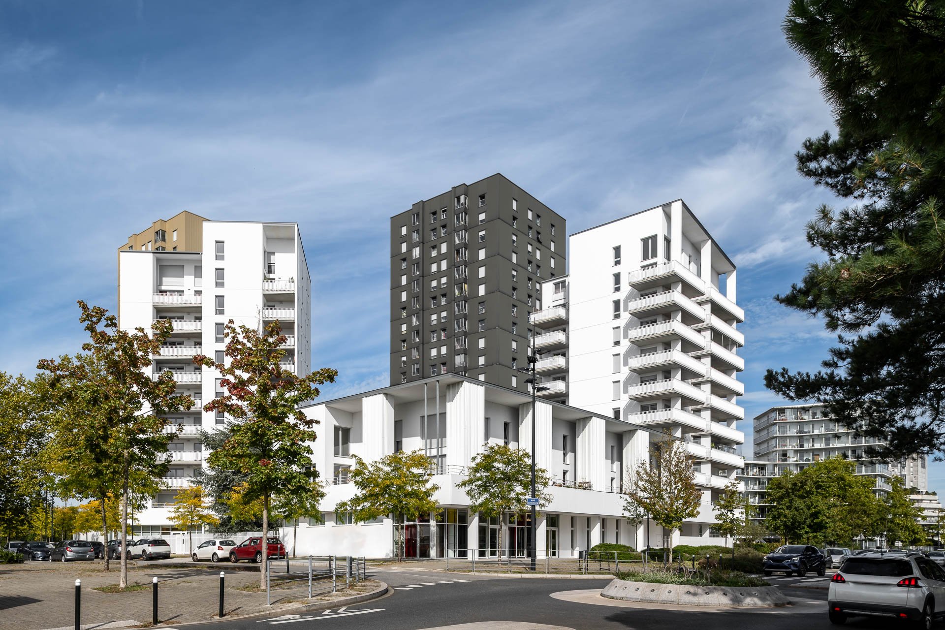 Bâtiments résidentiels modernes blancs et gris avec des balcons, arbres et voitures dans un environnement urbain