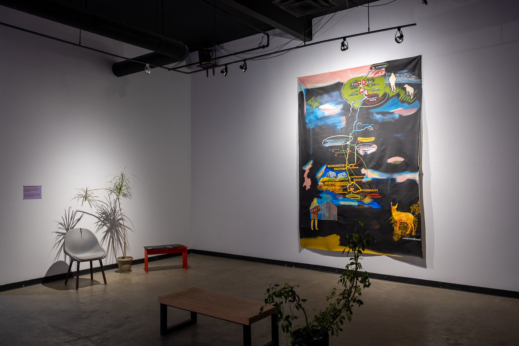  This is a wide view of the gallery, displaying Lauren Crazybull’s painted map. The map’s size can be compared to a chair sitting to the left of it - Crazybull’s map is about the height of three to four folding chairs stacked end to end, and as wide 
