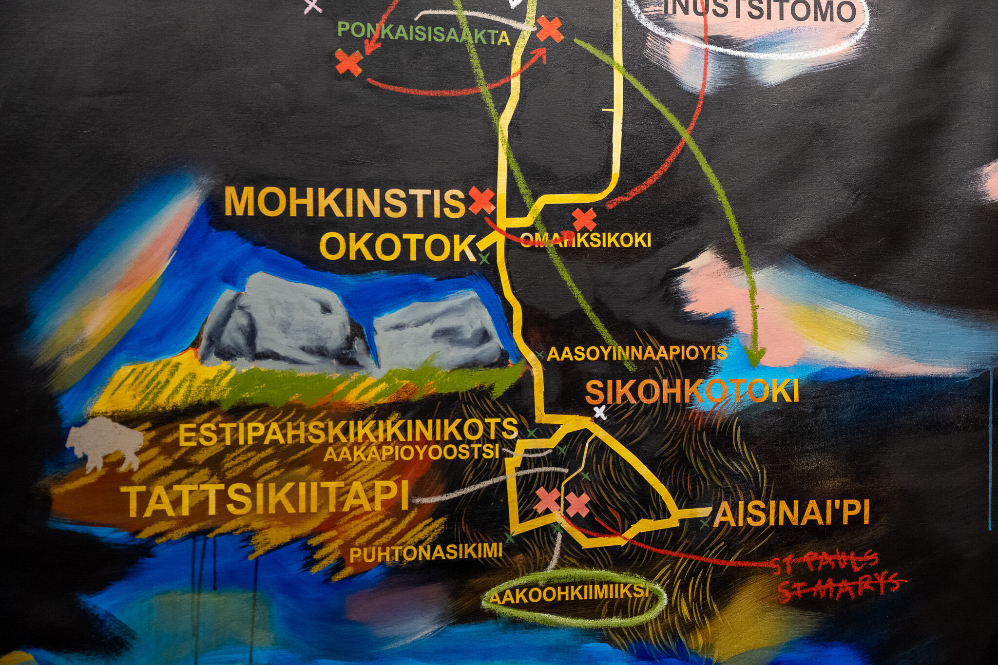  A close-up of Lauren Crazybull’s painted map. We have a closer look at yellow map lines that are in the lower half of the painting, along with a closer view of the painted rock formation, and the text that lists place names. In a circle of names nea