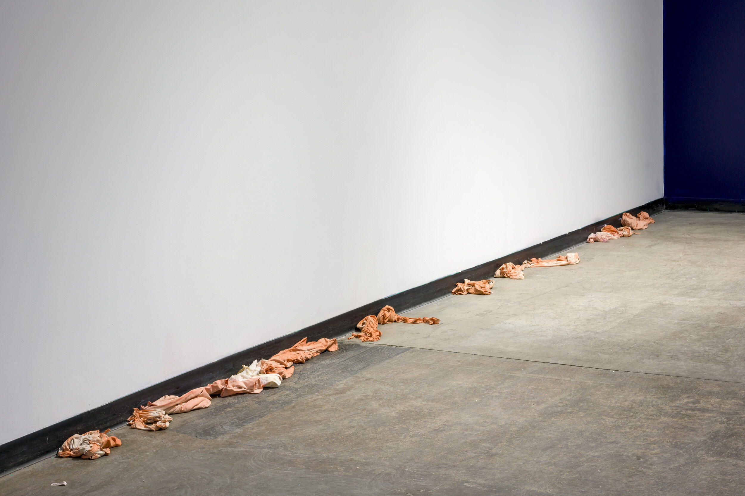  Pieces of crumpled orange and white fabric lay on the floor, pushed up against the wall. 