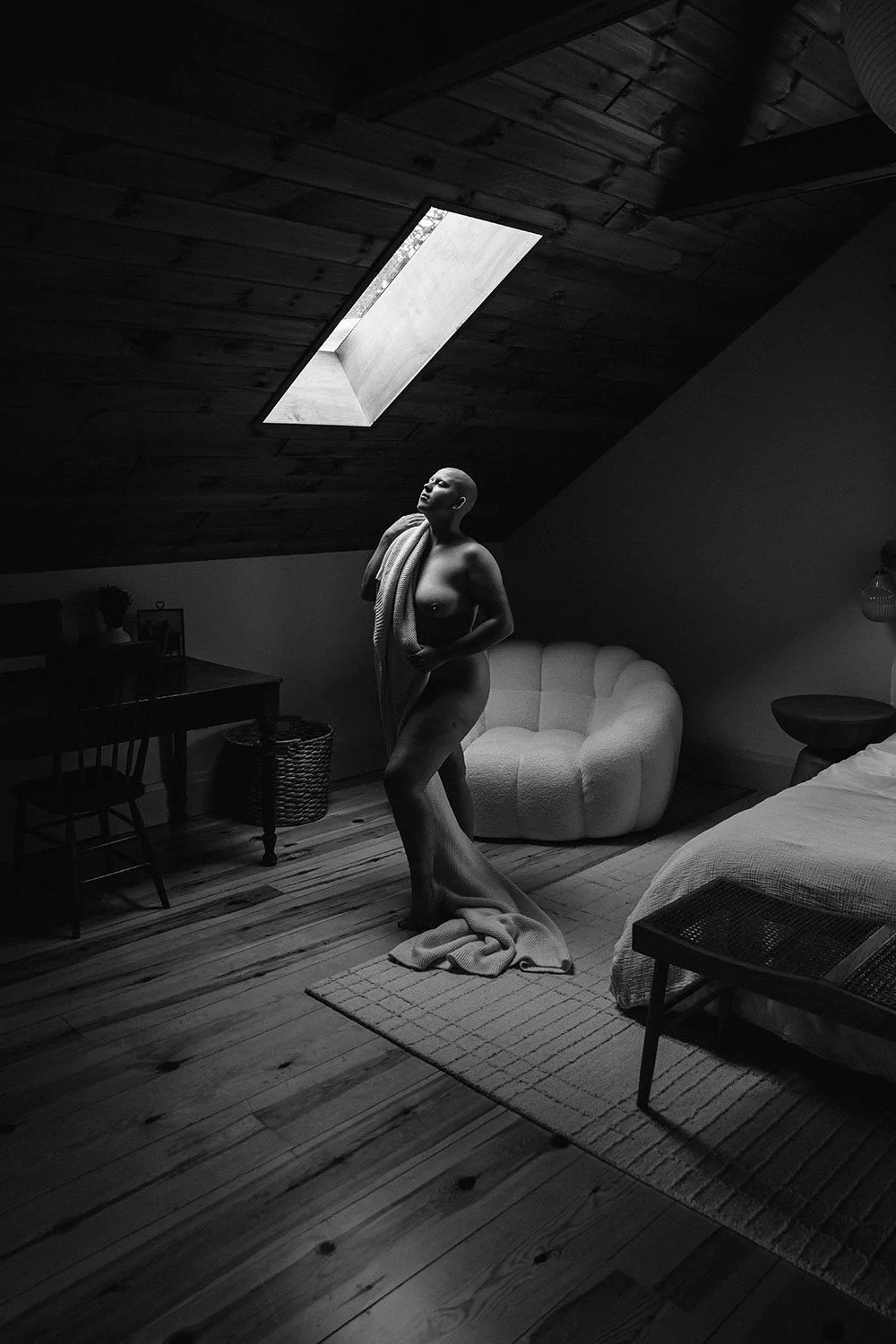 boudoir photography in hamilton ontario with a woman standing under a skylight holding a blanket