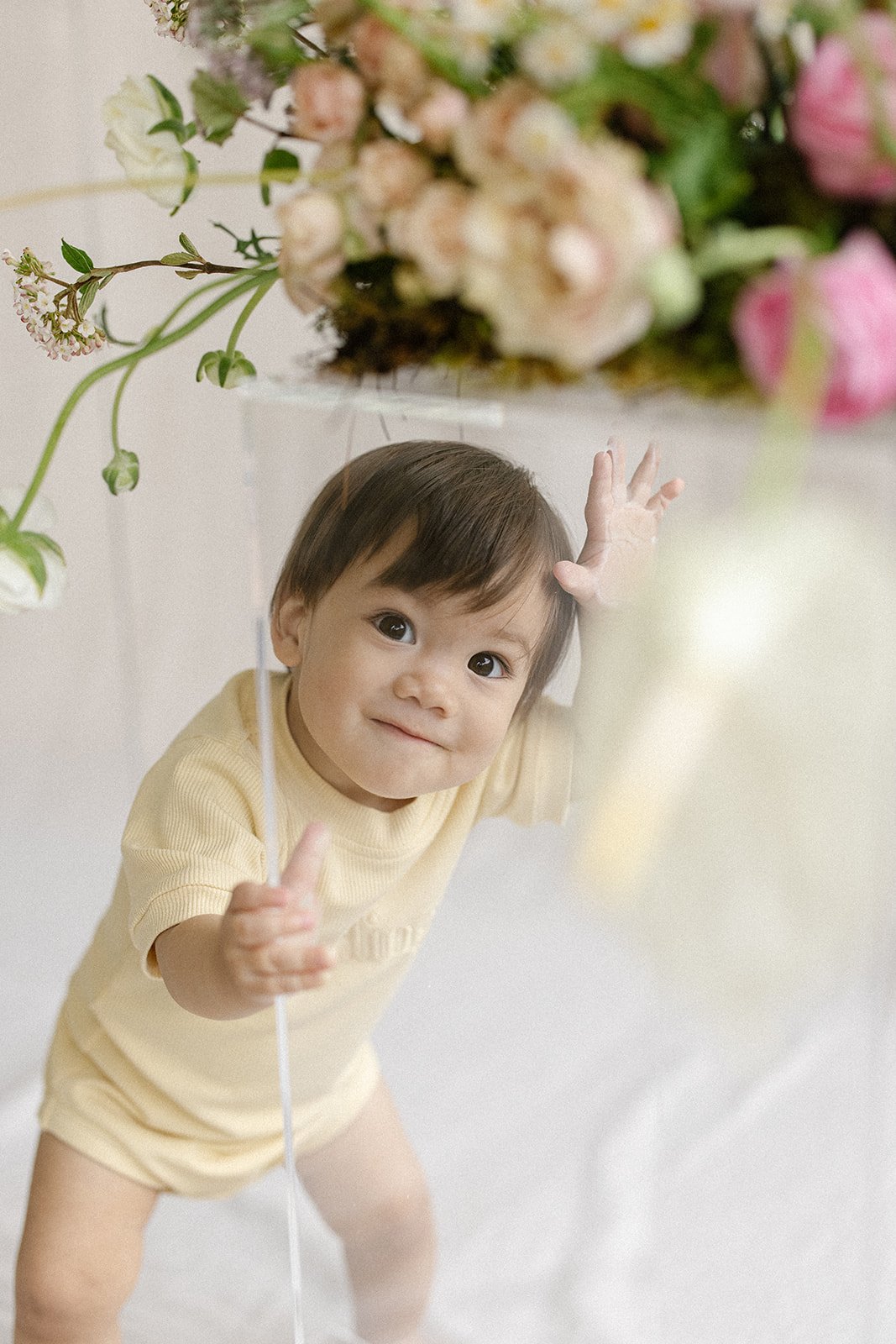 A cheeky little boy is hiding behind a clear plinth during a children's clothing brand shoot