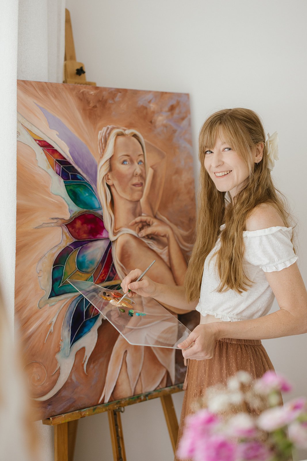 An artist with red hair is seen painting a fairy for her artist brand photoshoot