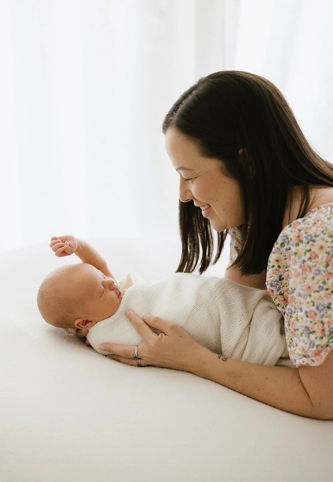 Mother holding and smiling at her newborn baby. Newborn baby wrapped in white blanket and holding his hand to the sky.