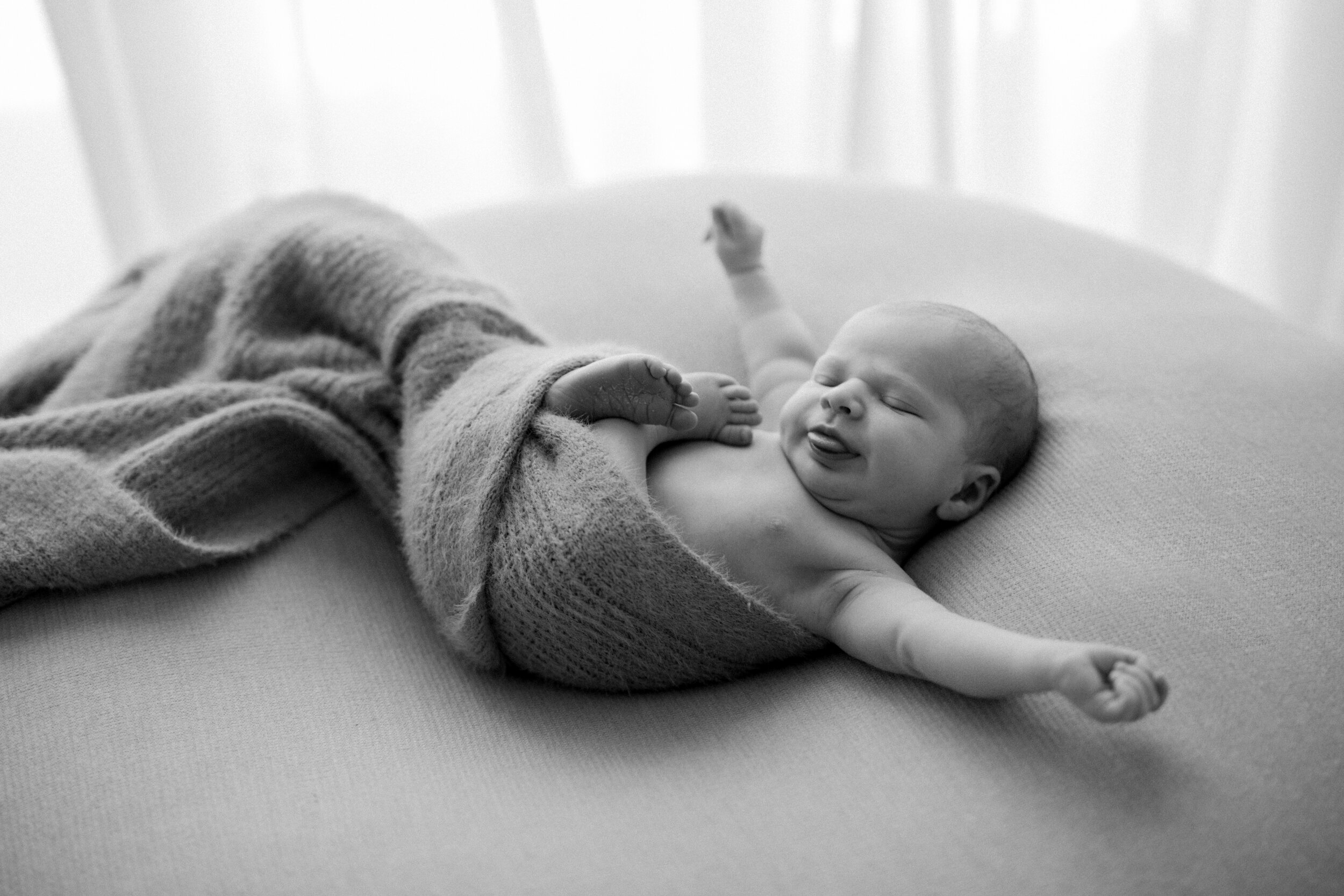curled up newborn baby stretching it's arms