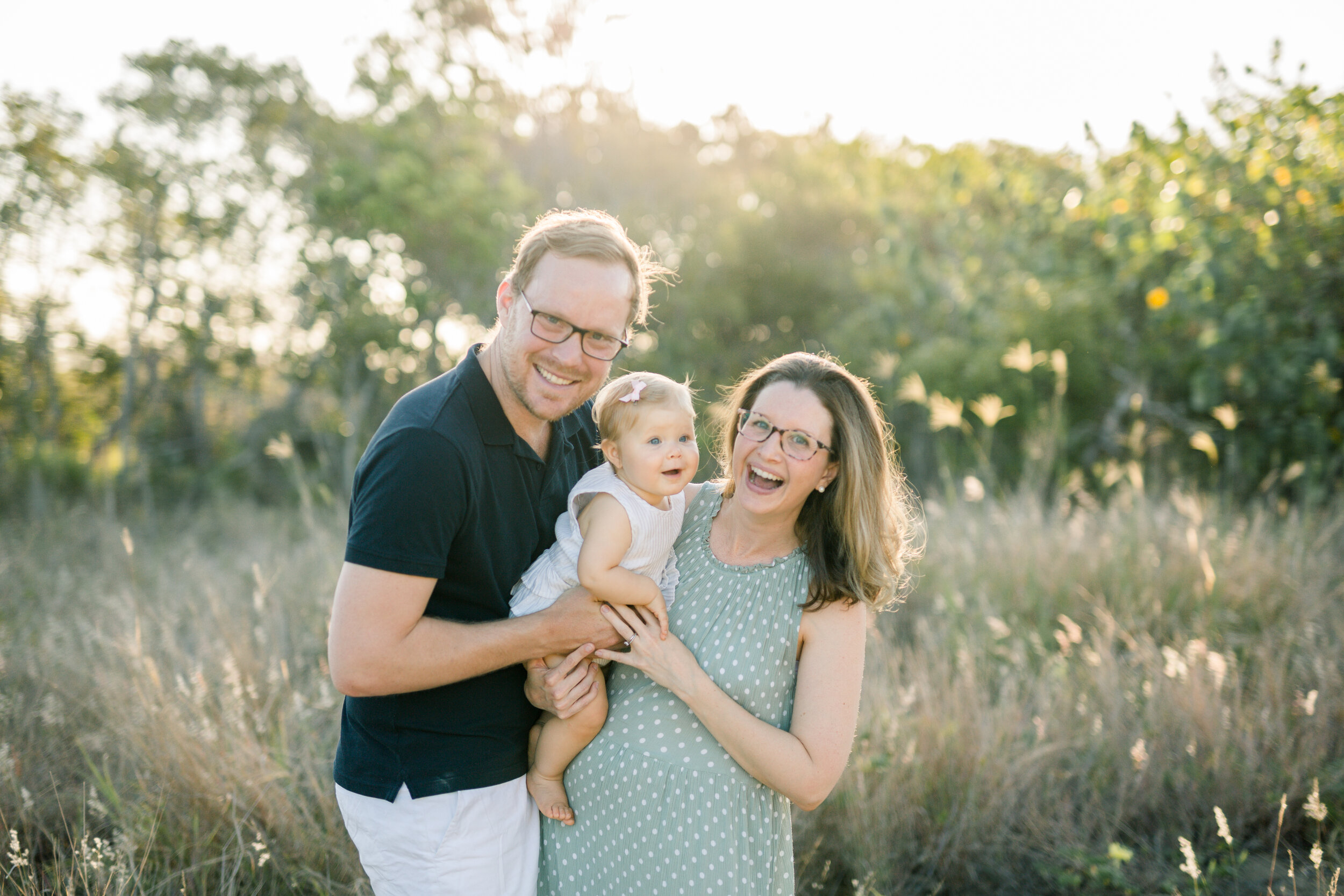 Happy family playing in the long grass at sunset