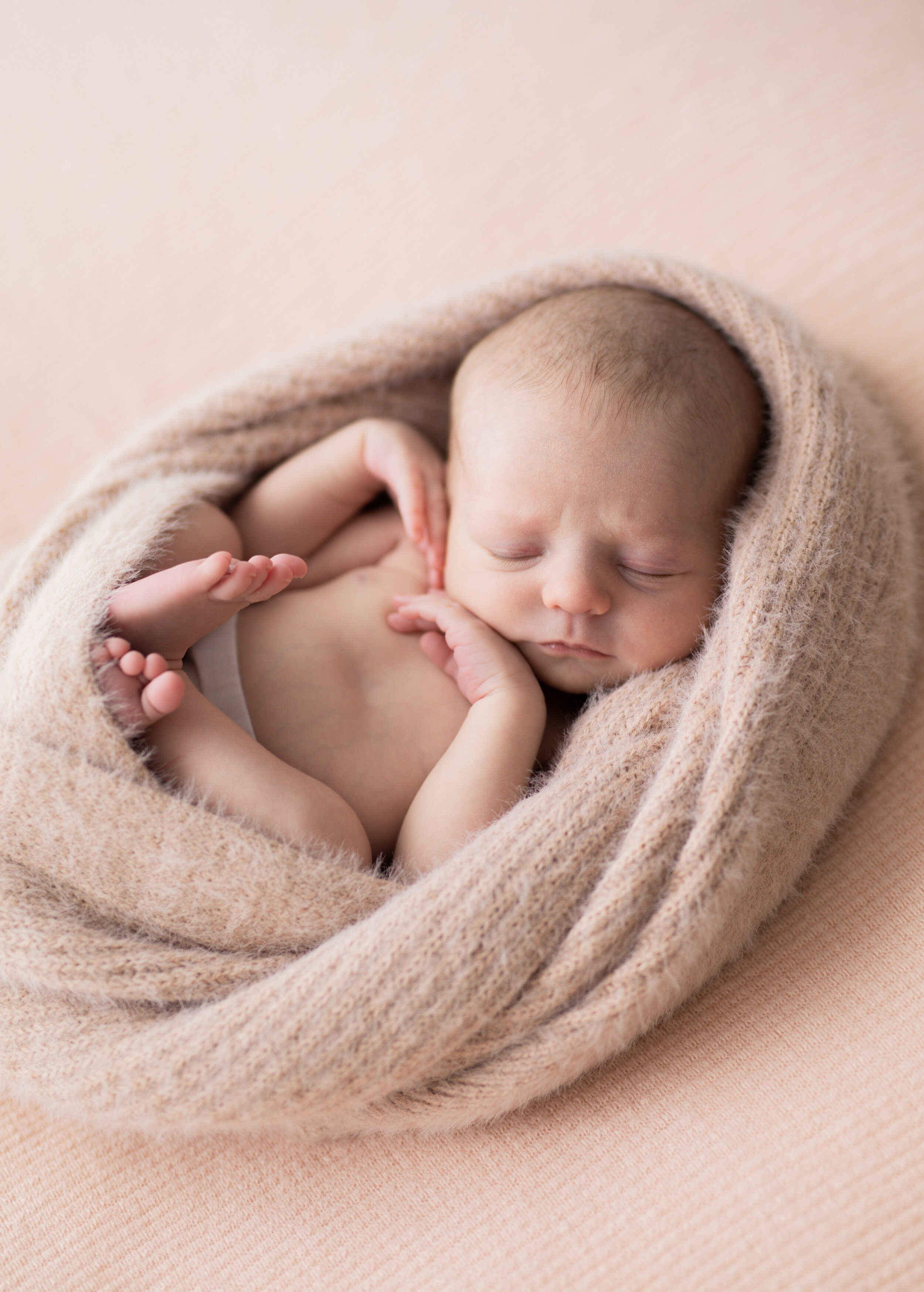 tiny newborn snug in a pink fluffy wrap