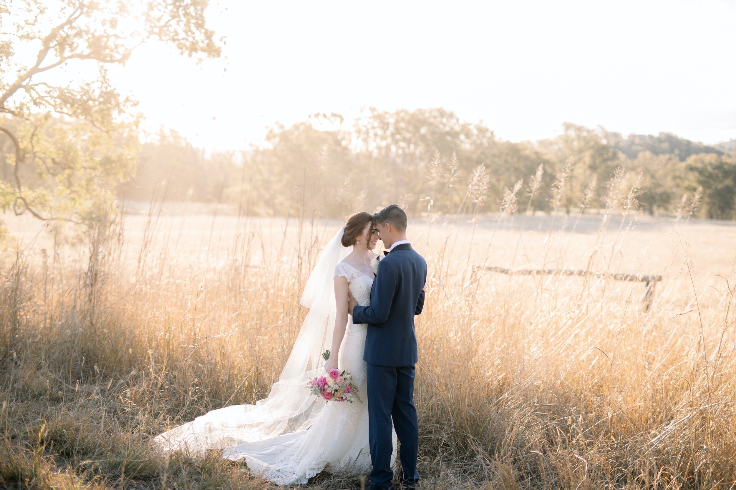 Groom holding his Bride close near an open field