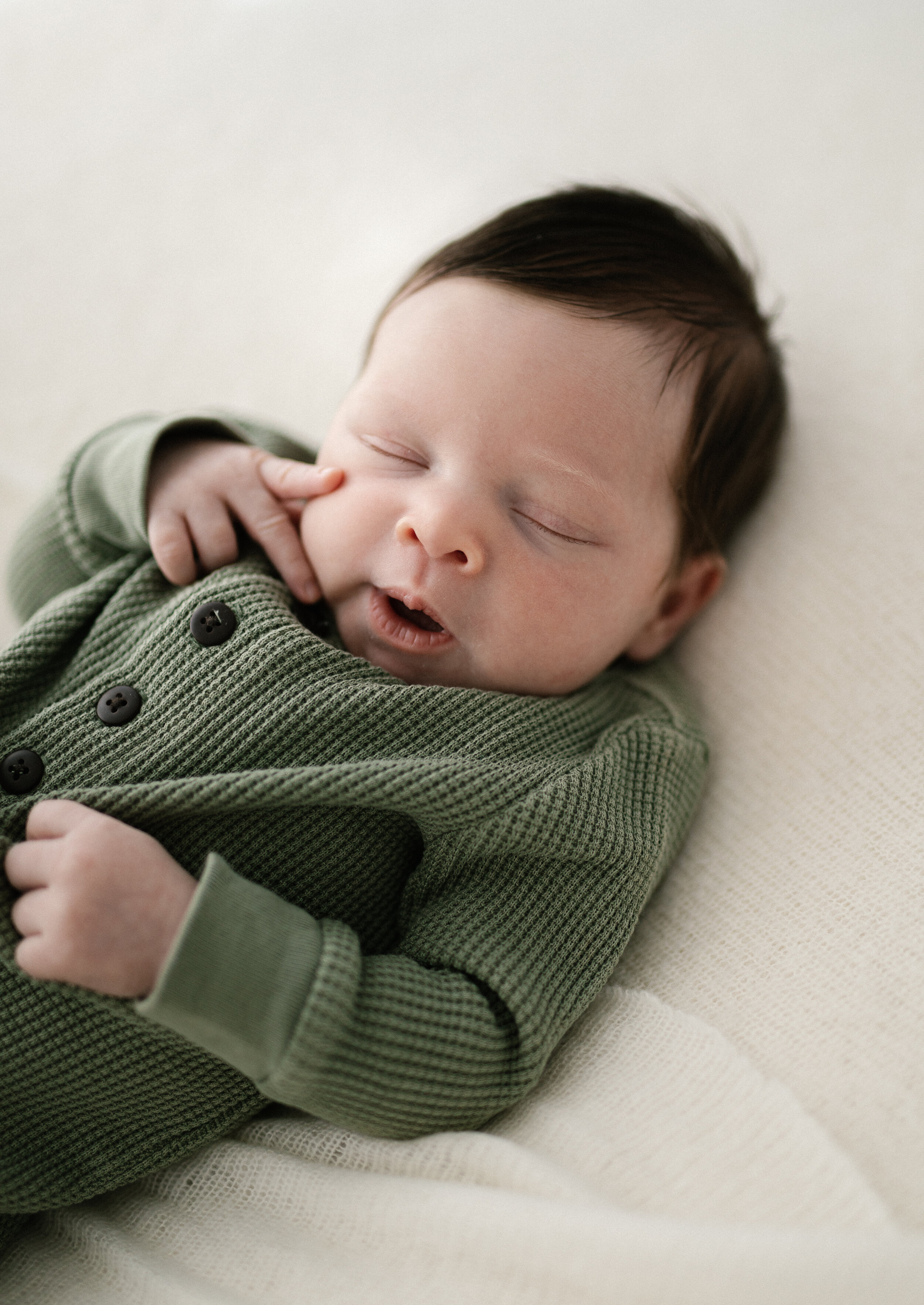 Newborn baby girl dressed in forest green romper just about to yawn 