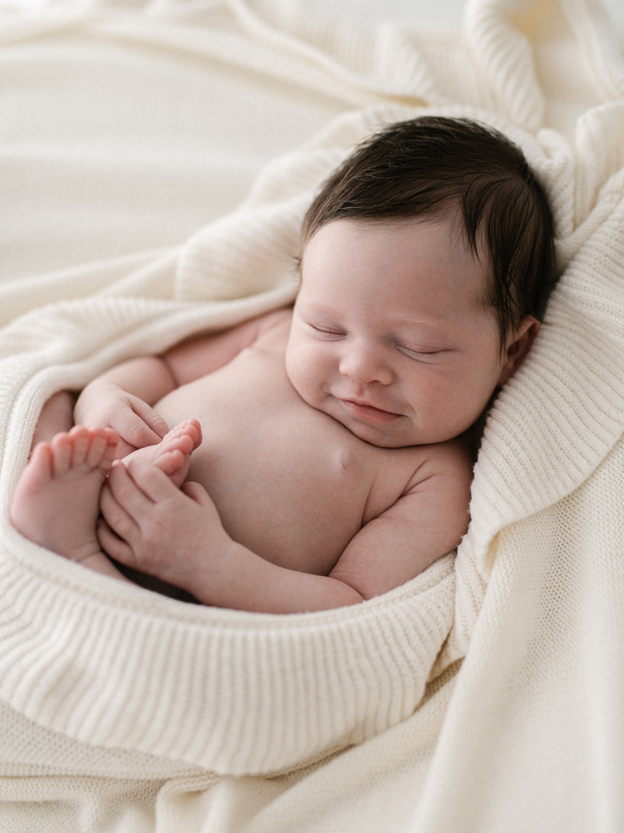 newborn baby girl with beautiful dark hair wrapped in a soft cream ruffle blanket