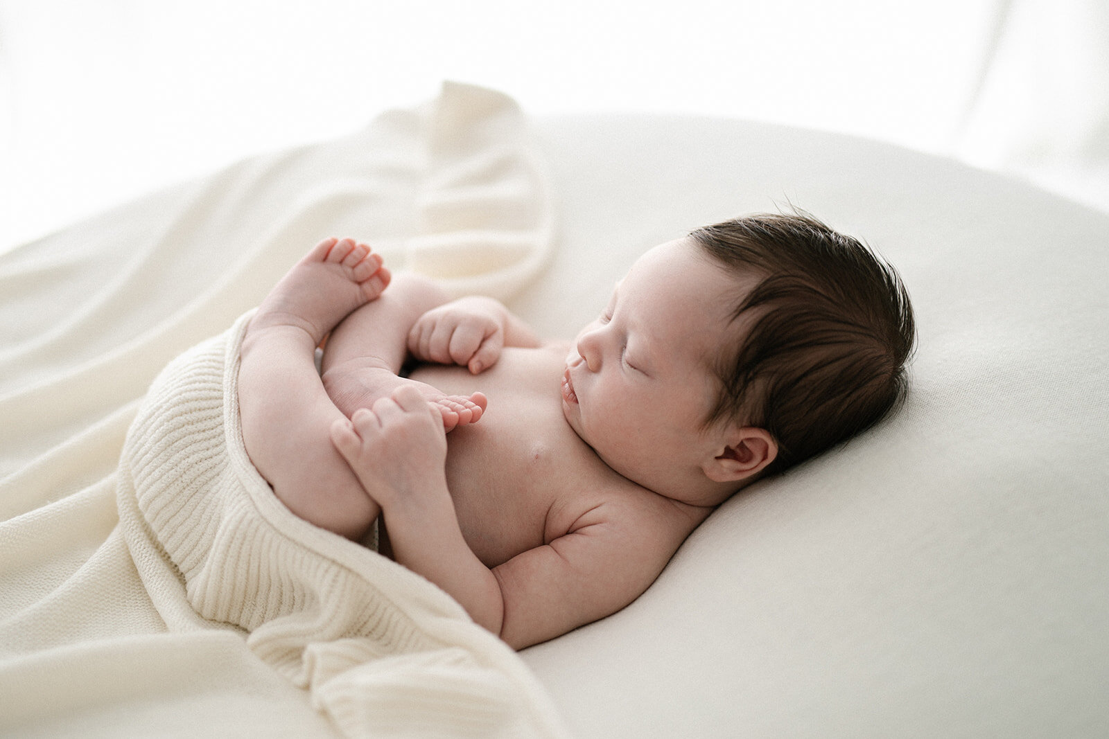 newborn baby girl cuddled up with white ruffle blanket