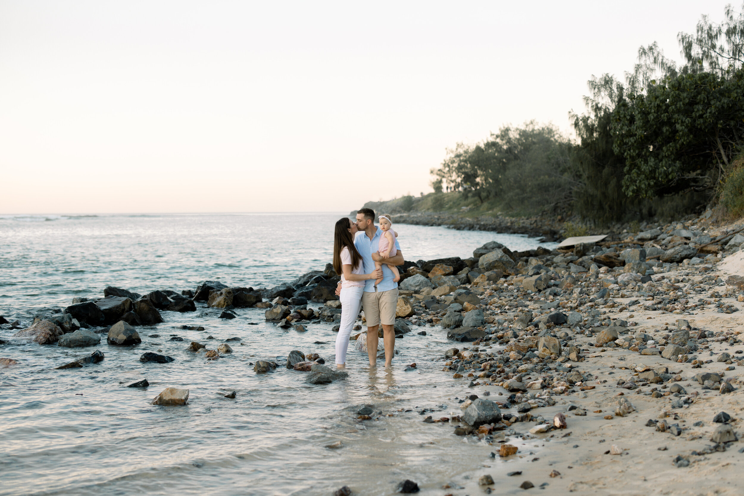 Couple kissing on the rocky beach holding their daughter