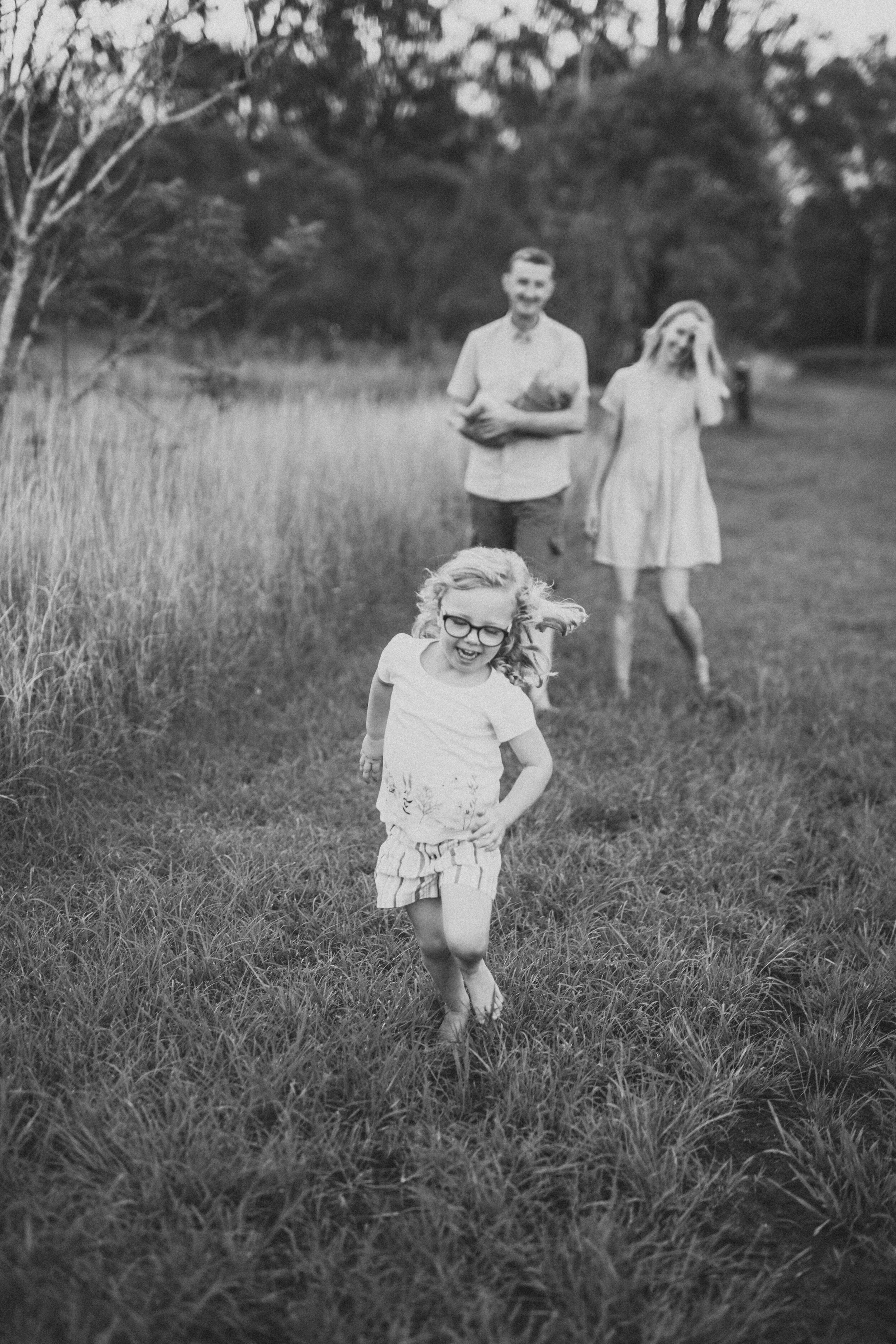 Little girl running in the grass with her family behind her