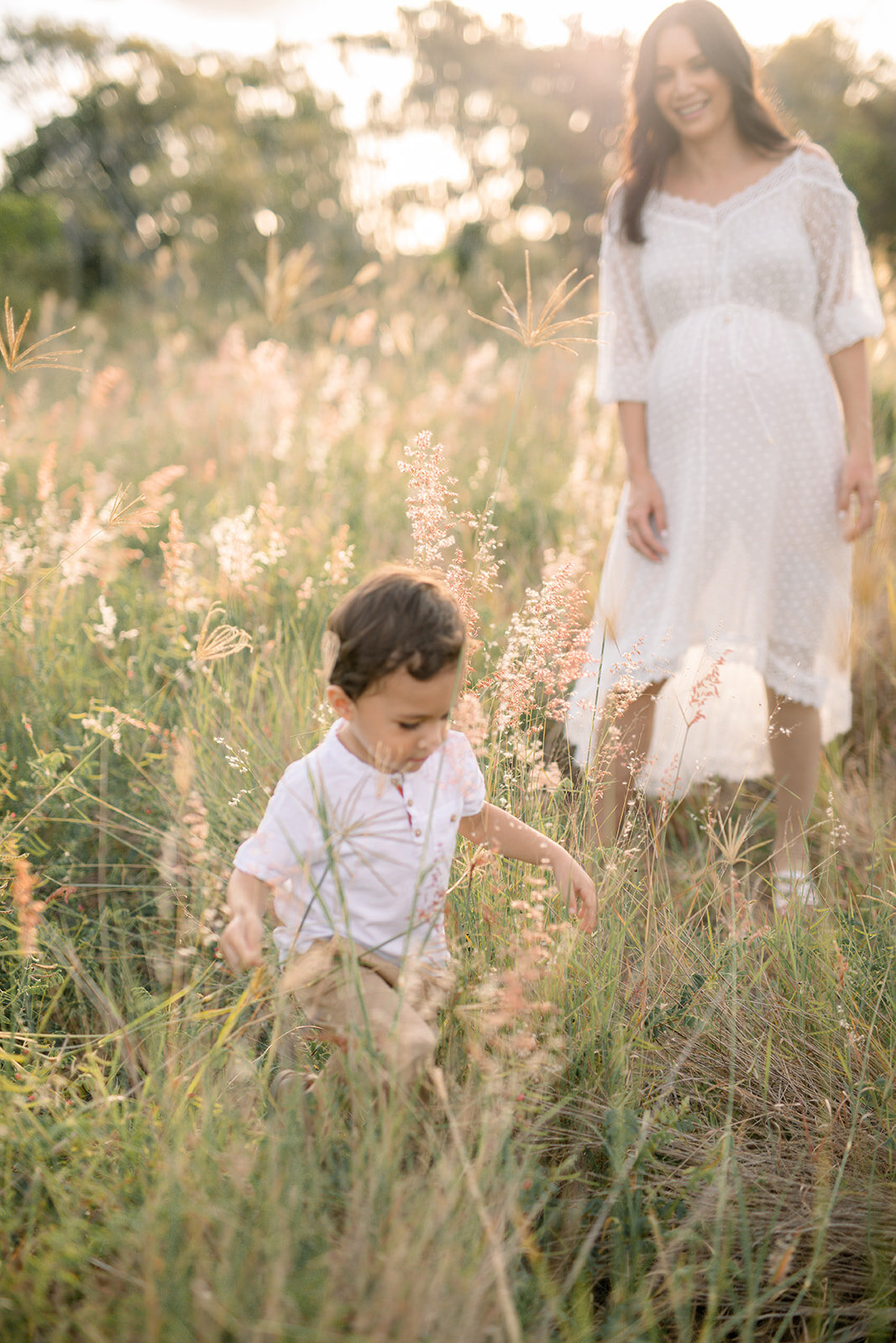 Young boy running in the golden grass with his mother 