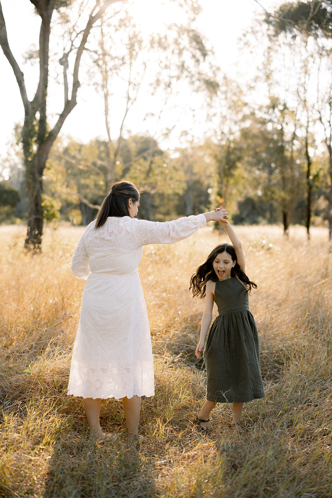 Mother in a white dress twirling her daughter in a field