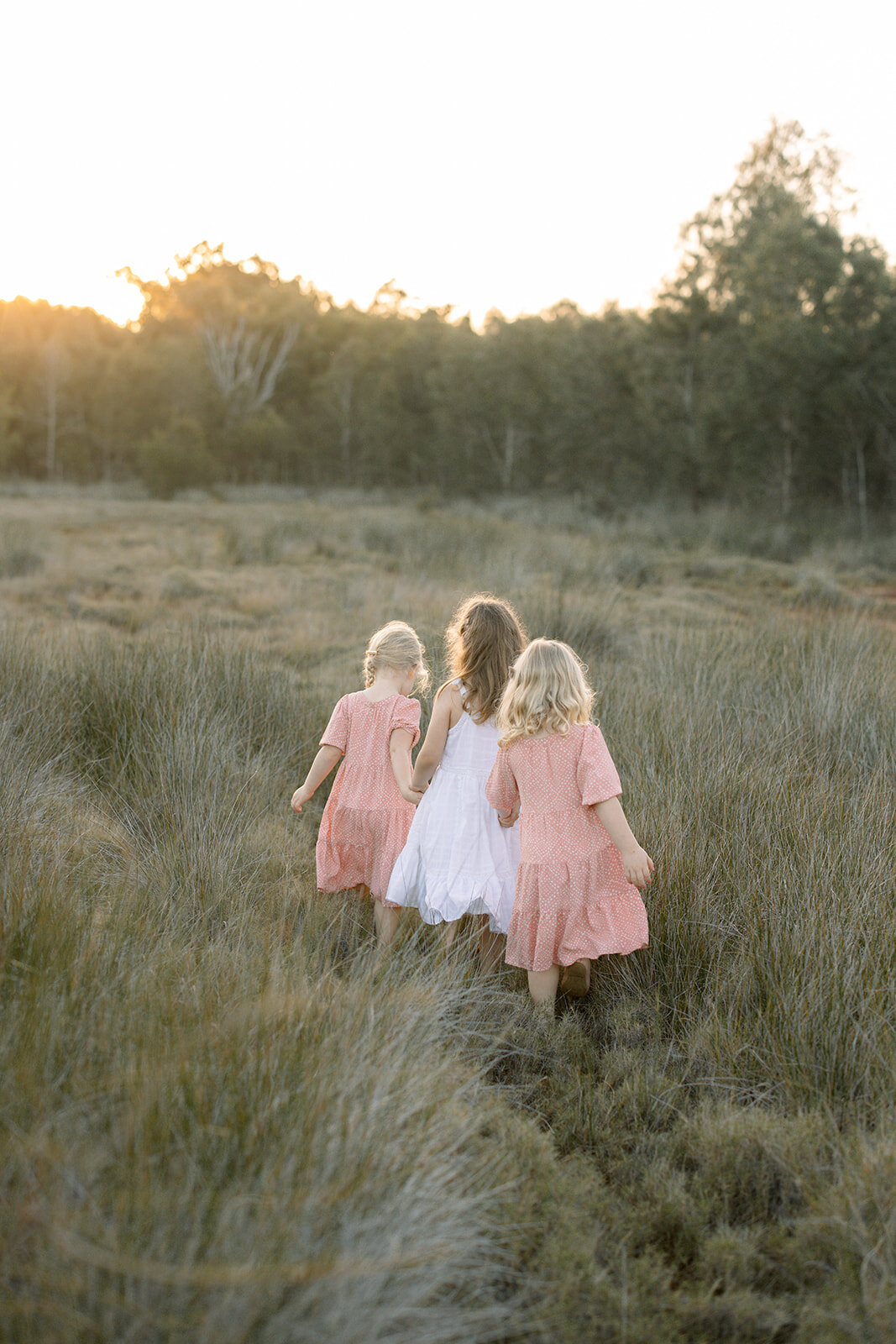 Three sisters walking through the grass at sunset