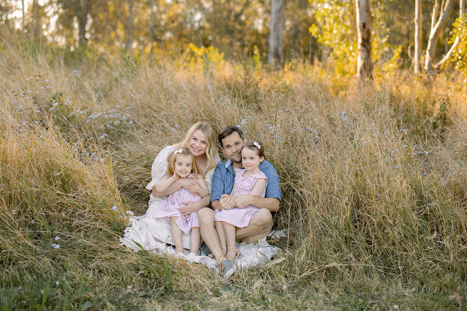 Twin sisters sitting with their mum and dad in the long grass