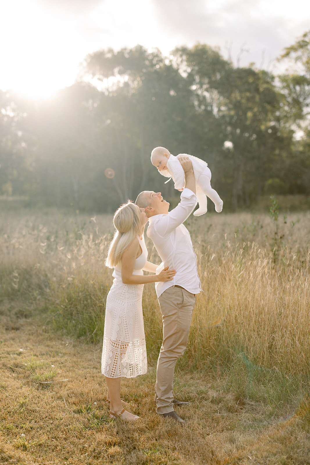 Dad lifting his baby girl in the air in a golden field