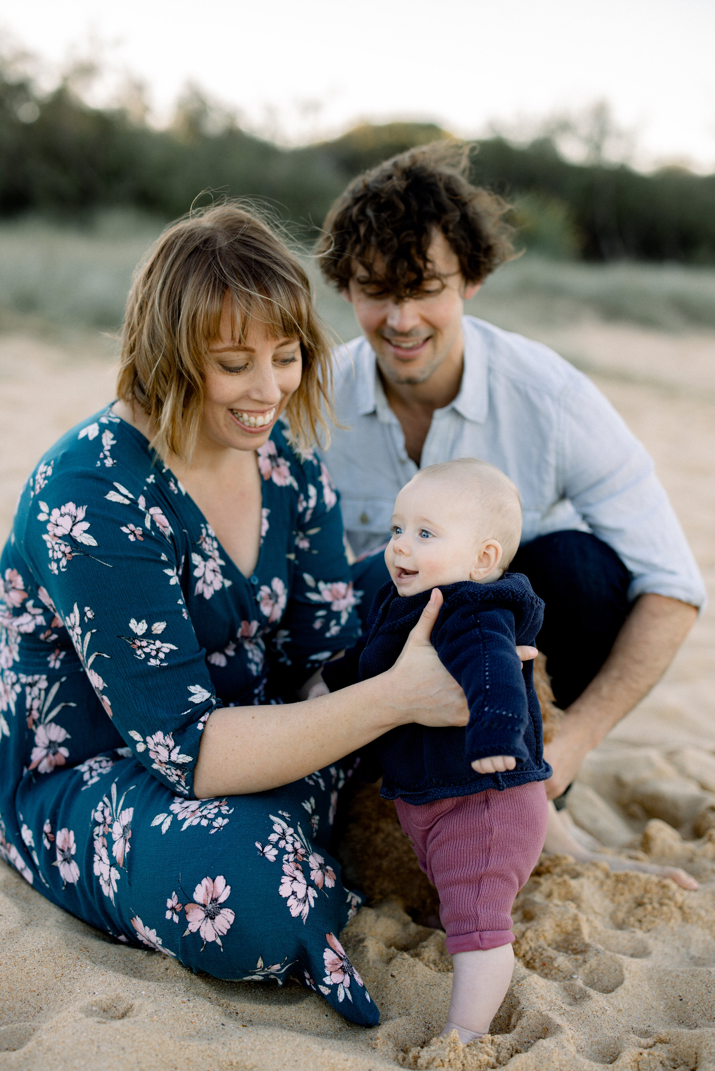 Baby girl standing in the sand with her Mum and Dad