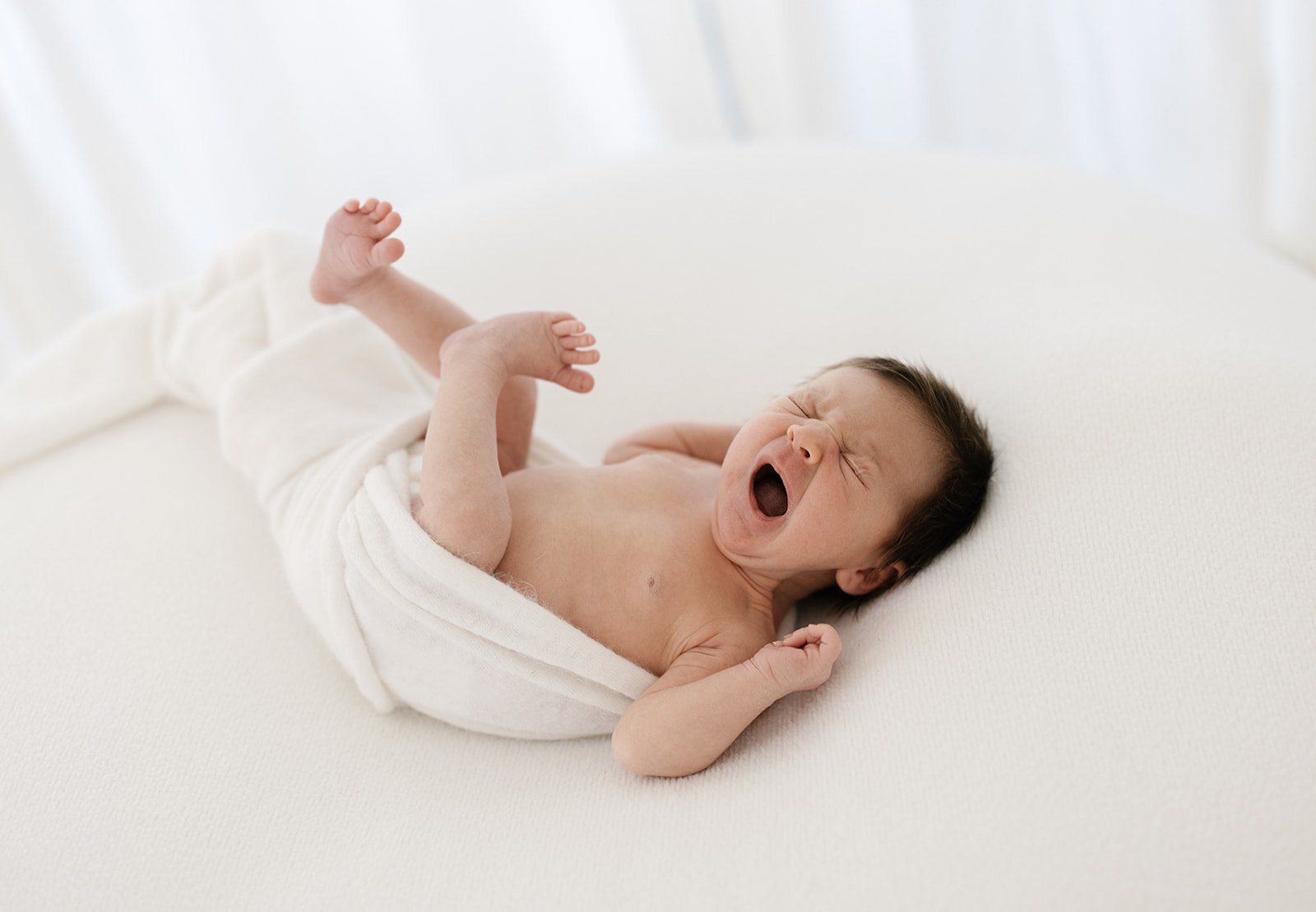 brisbane newborn baby yawning while wrapped in a white wrap