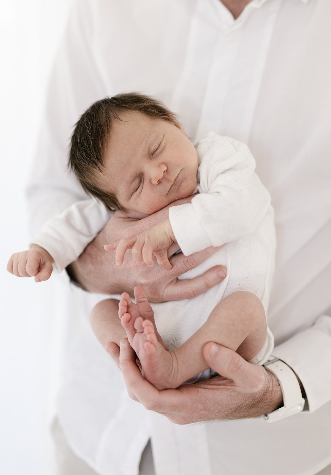 newborn baby with dark hair stretches in her fathers arms