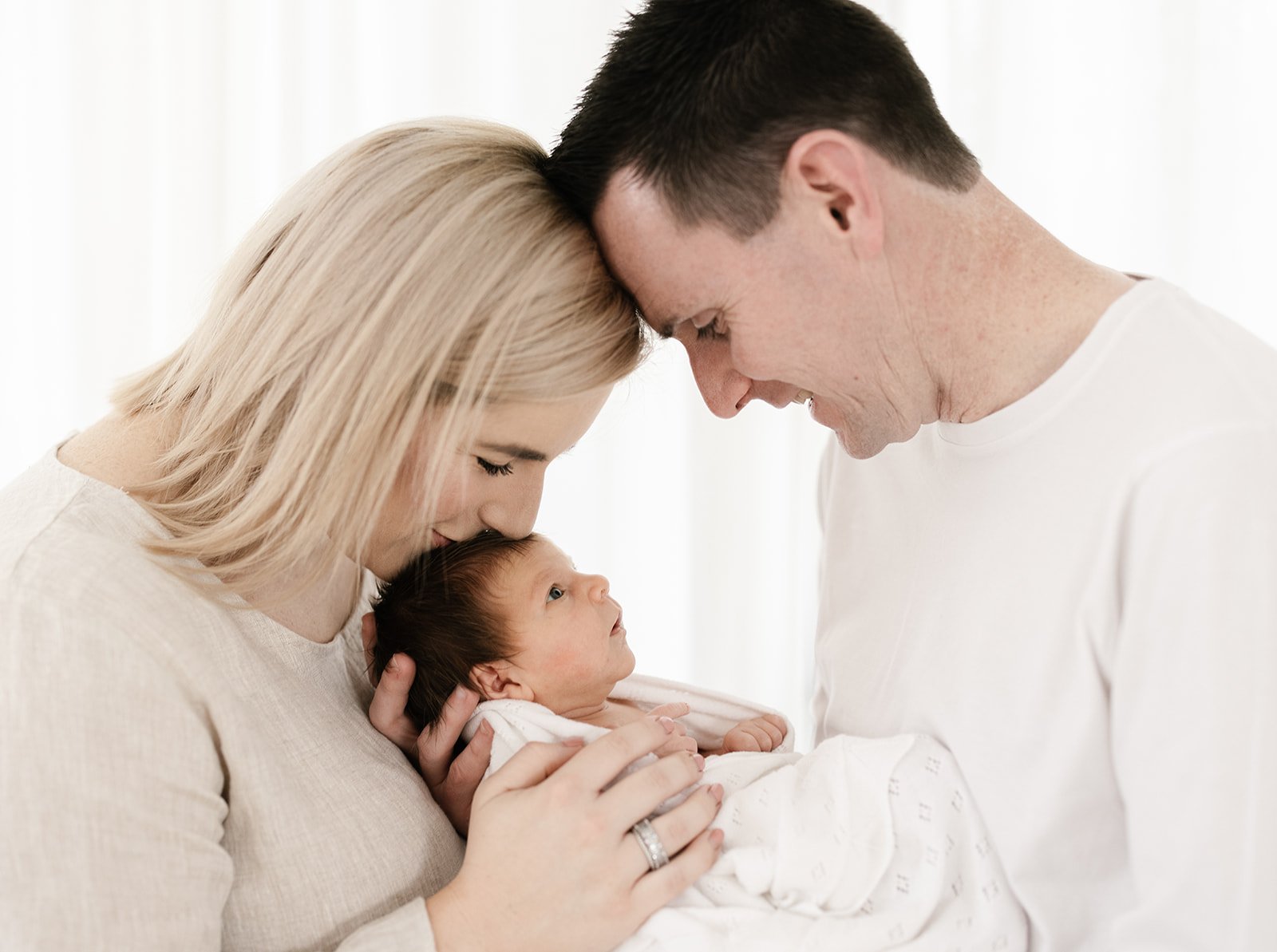 blonde mother and dark hair father look lovingly over their newborn baby girl
