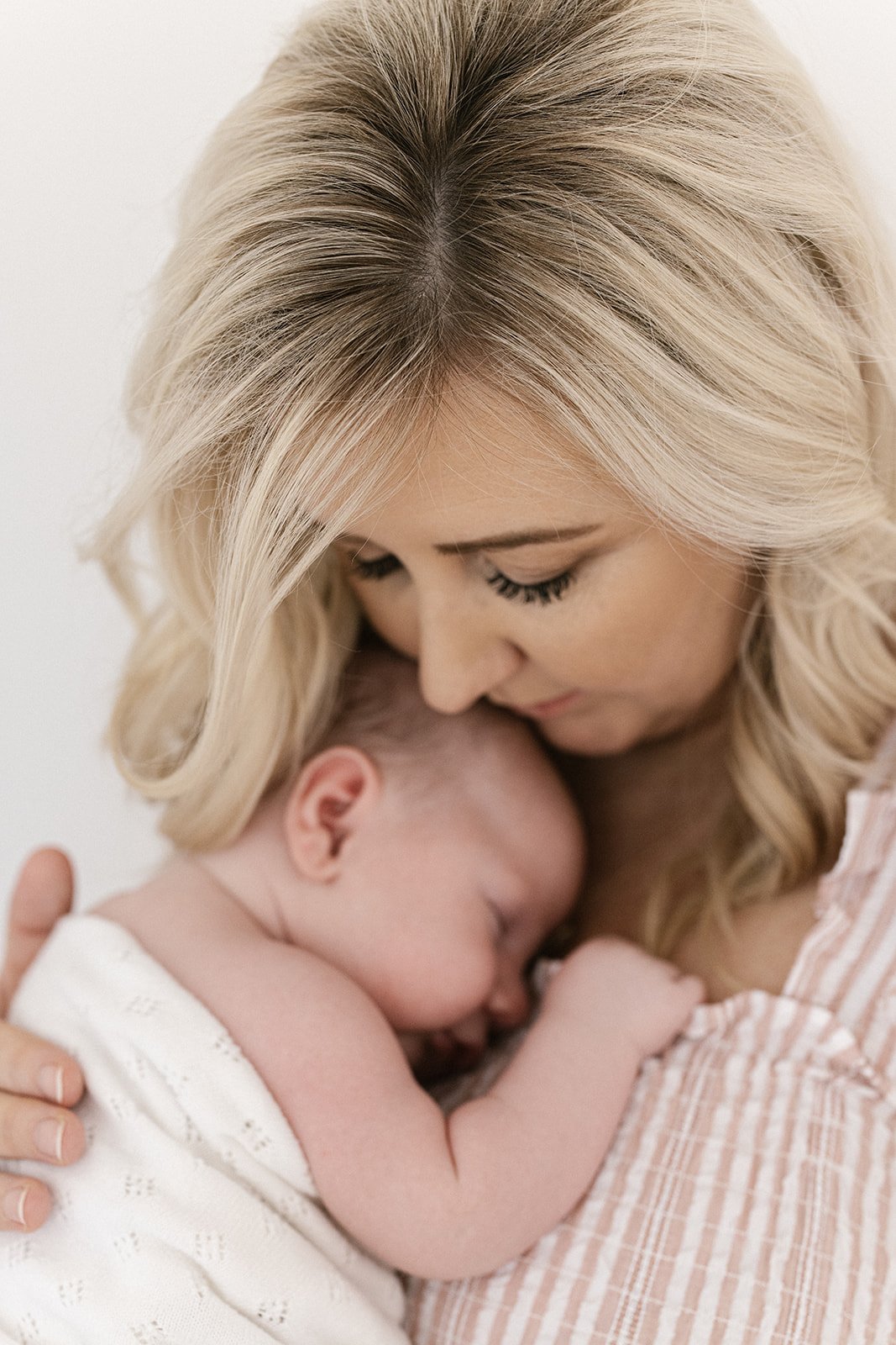 blonde mother in a pink stripped dress cuddles her fresh newborn 