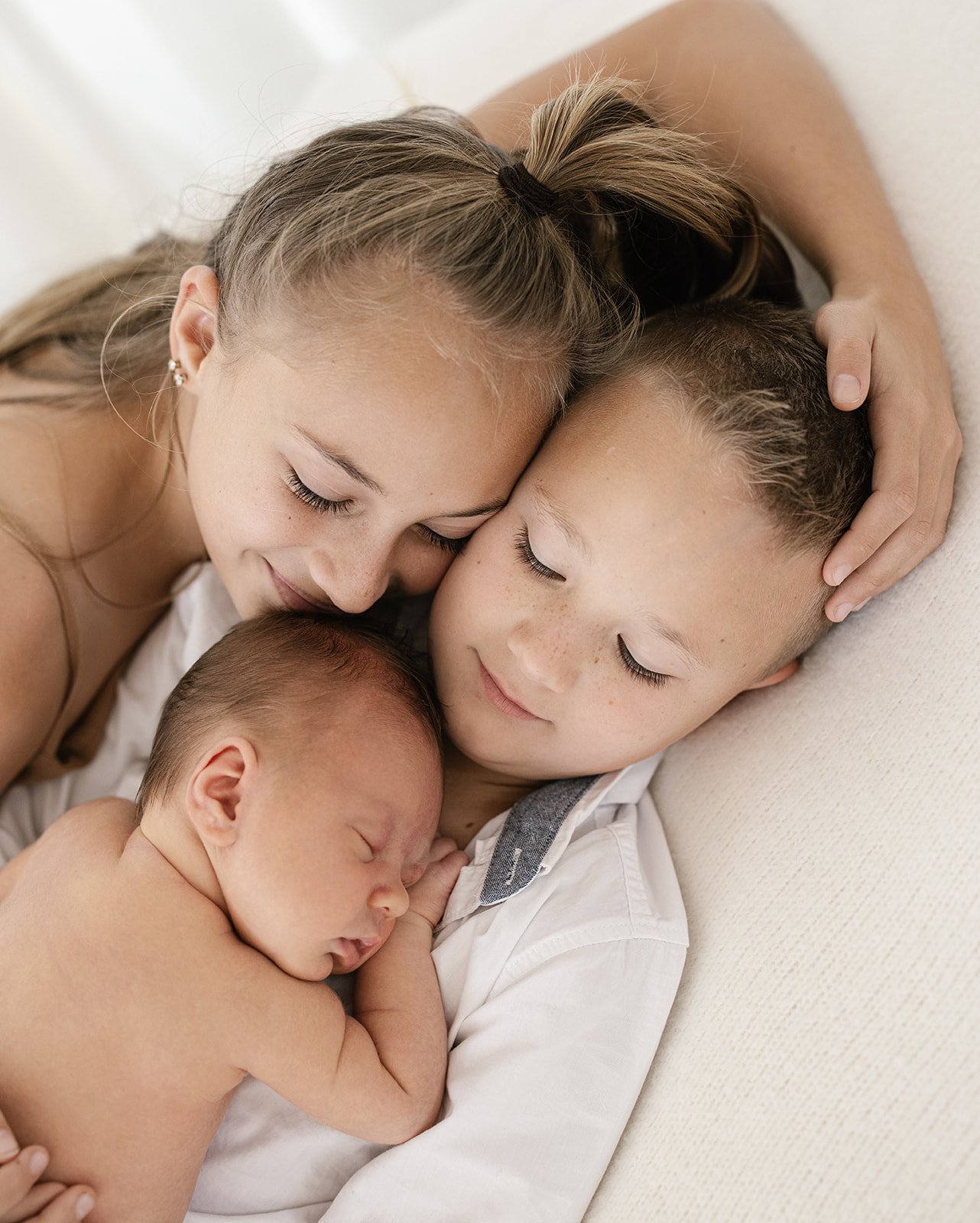 three siblings cuddled up together with their eyes shut