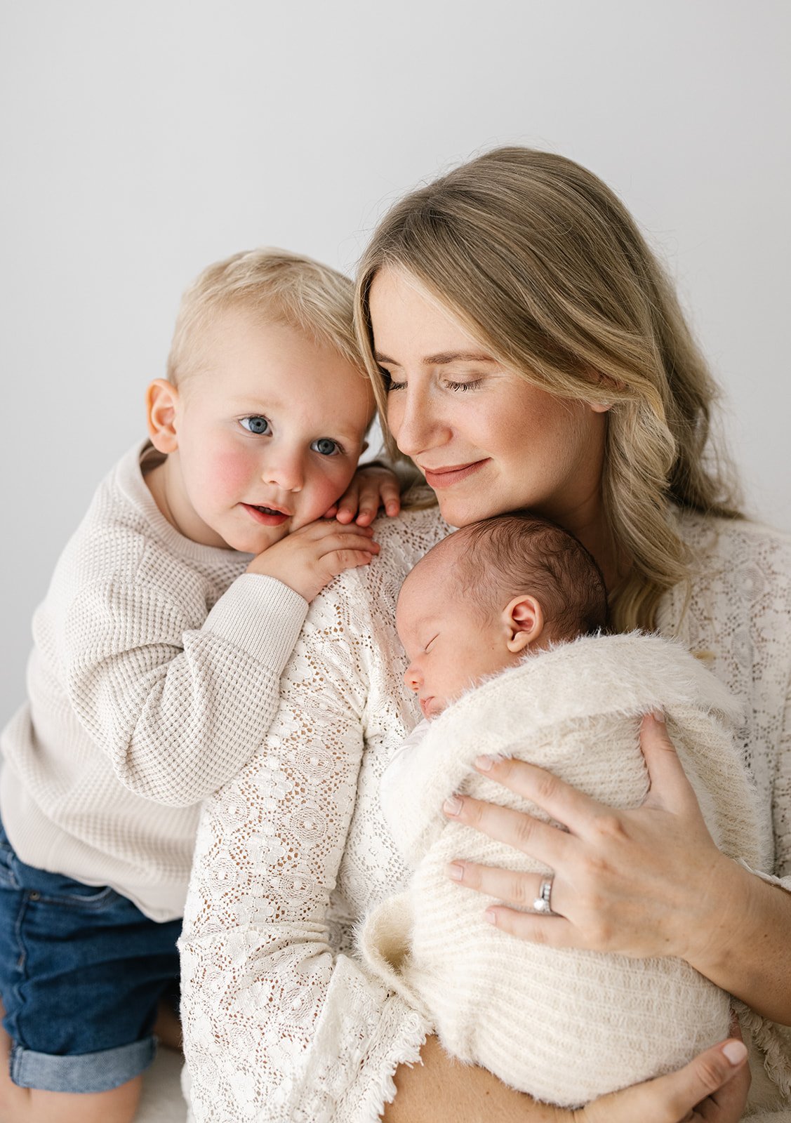 Blonde Brisbane mother snuggles into her newborn baby while her older toddler cuddles into her shoulder