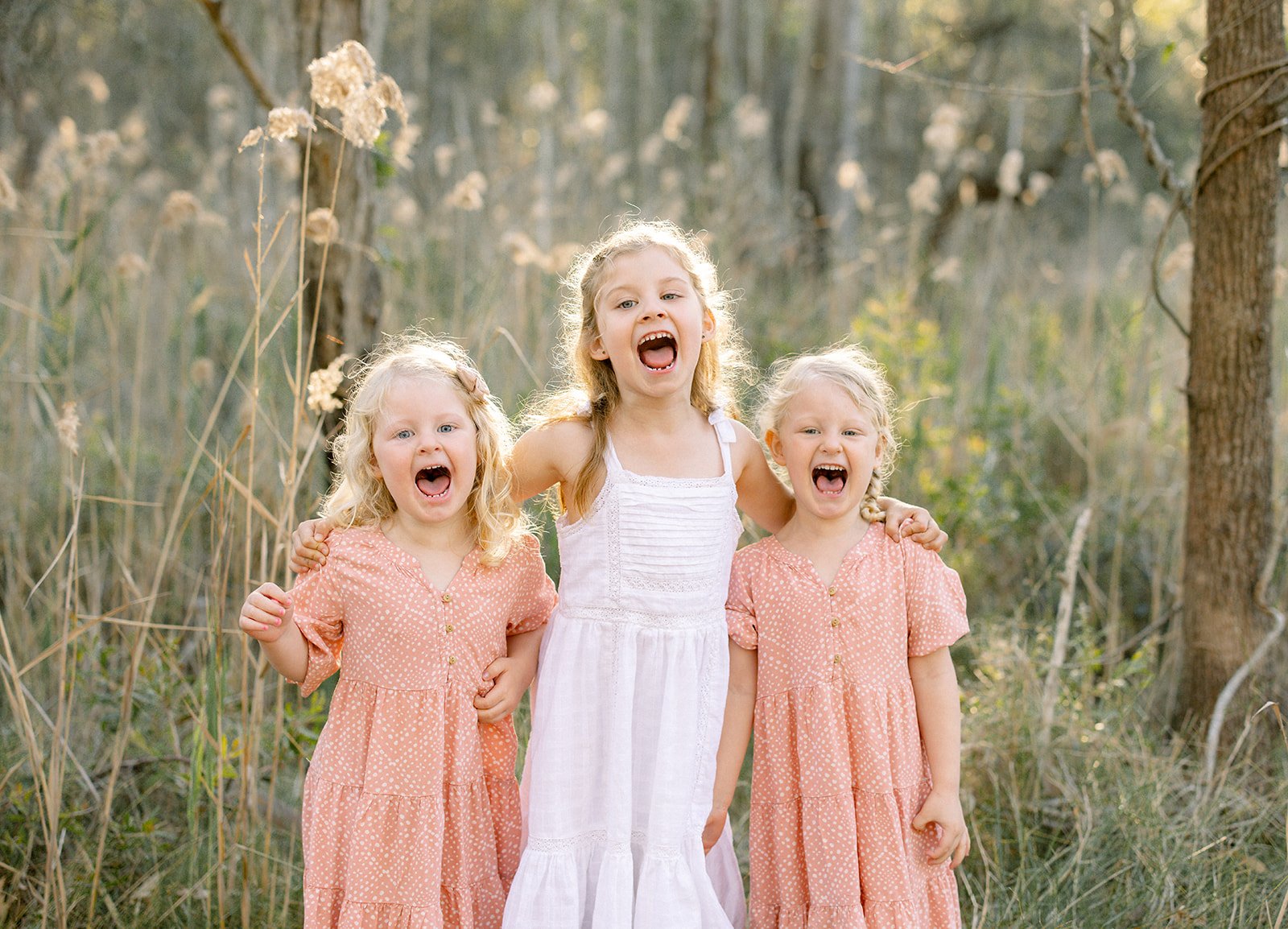 Three sisters standing togther laughing in white and pink dresses