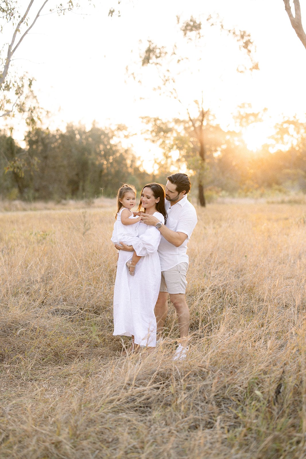 Family standing together in a golden grassy field at sunset