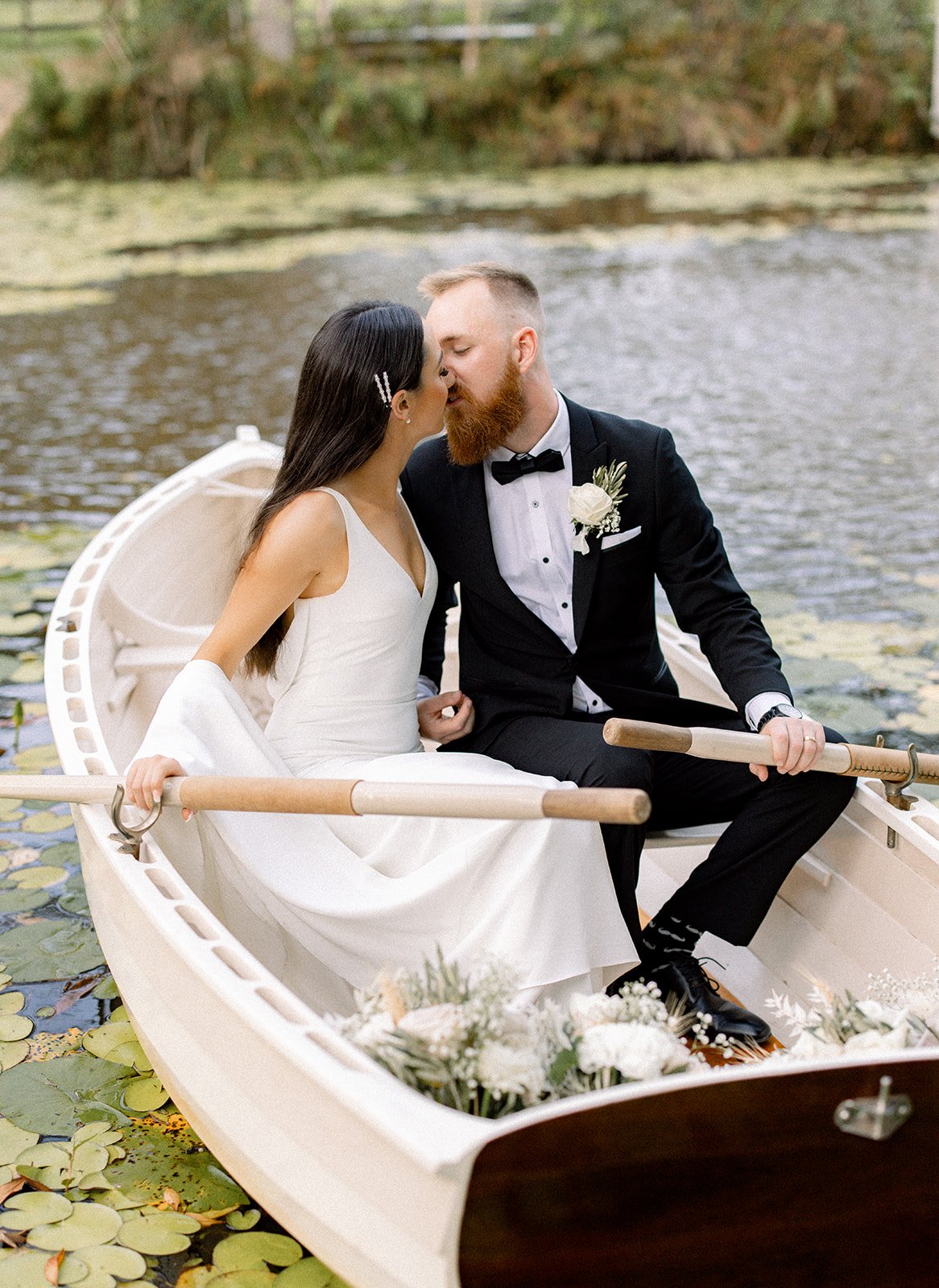 a bride and groom kiss in a wooden row boat