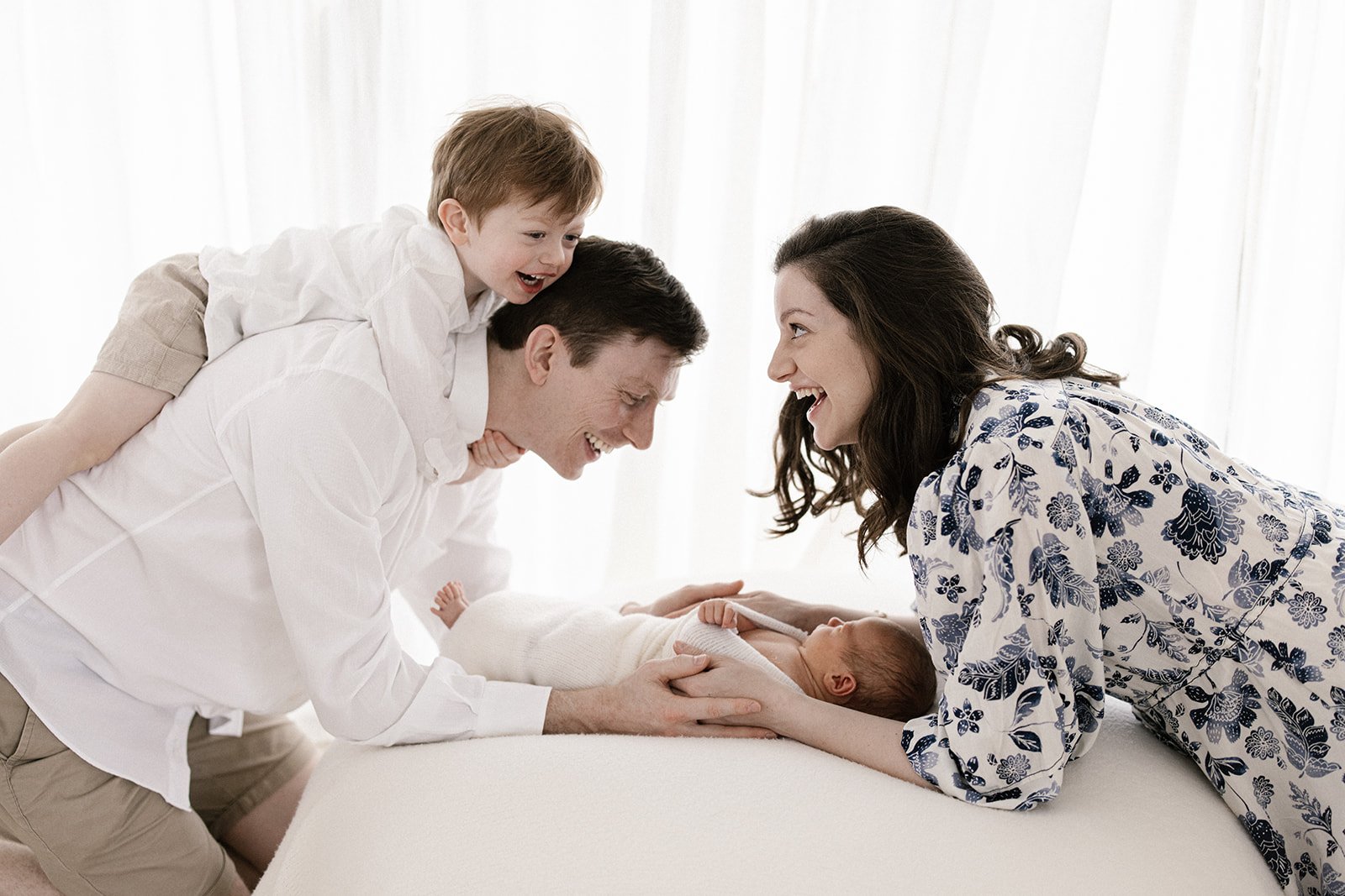 Brisbane family looking over their newborn baby while toddler climbs on dads back