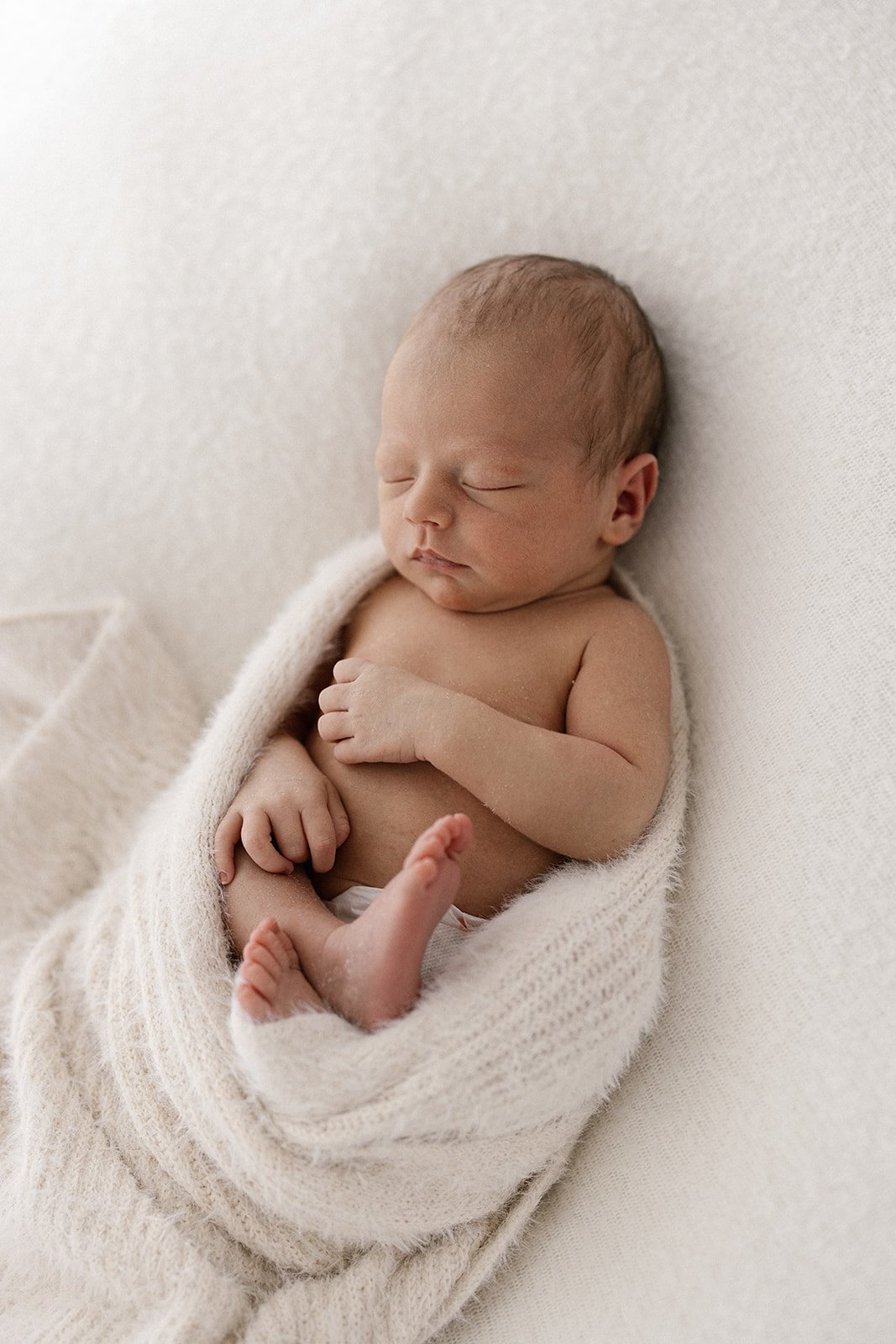 baby curled up in a fluffy cream wrap