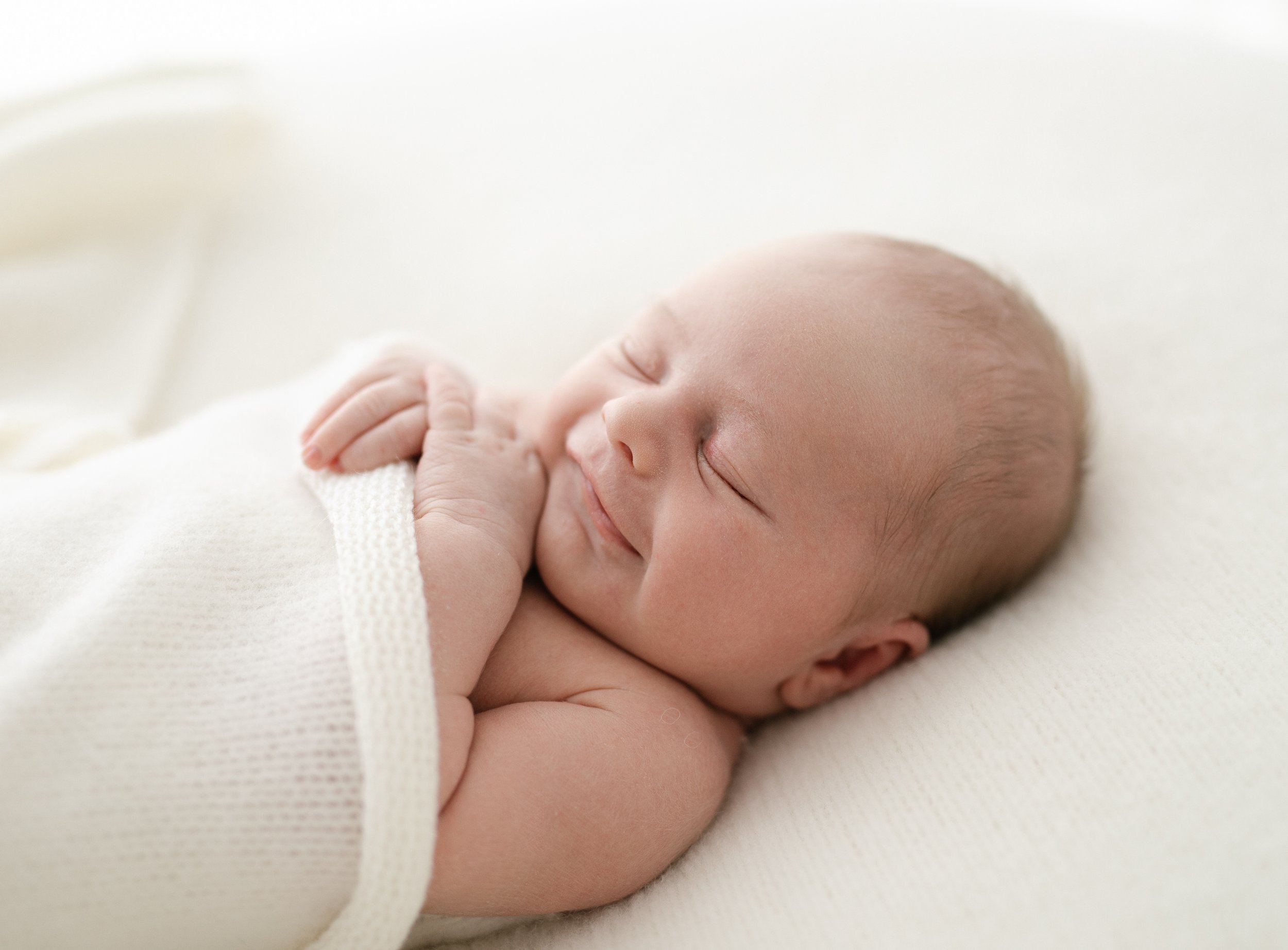 newborn baby smiles while wrapped in cream white blanket