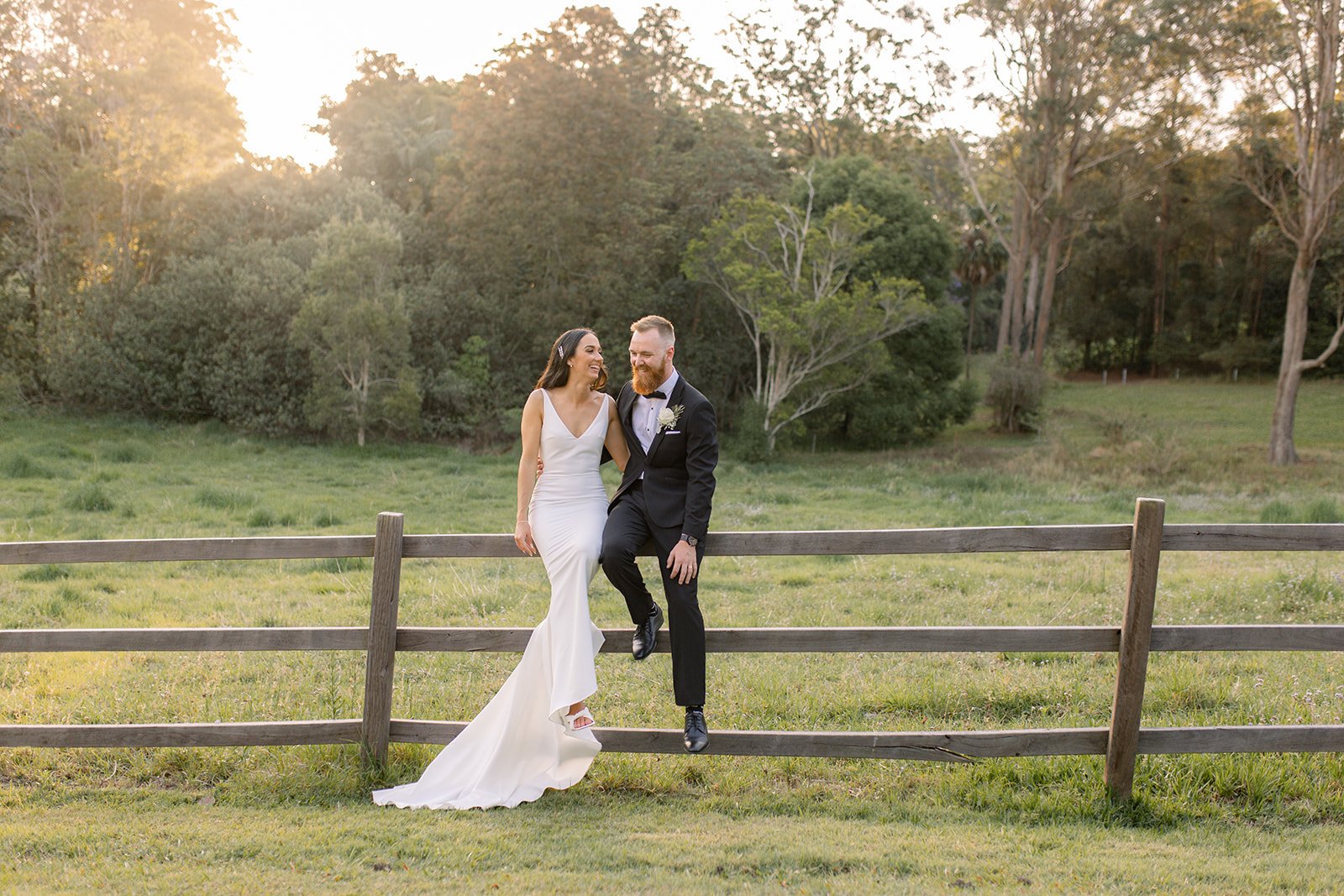 Sunshine Coast bride and groom sitting on a wooden fence with a glowing sunset behind them