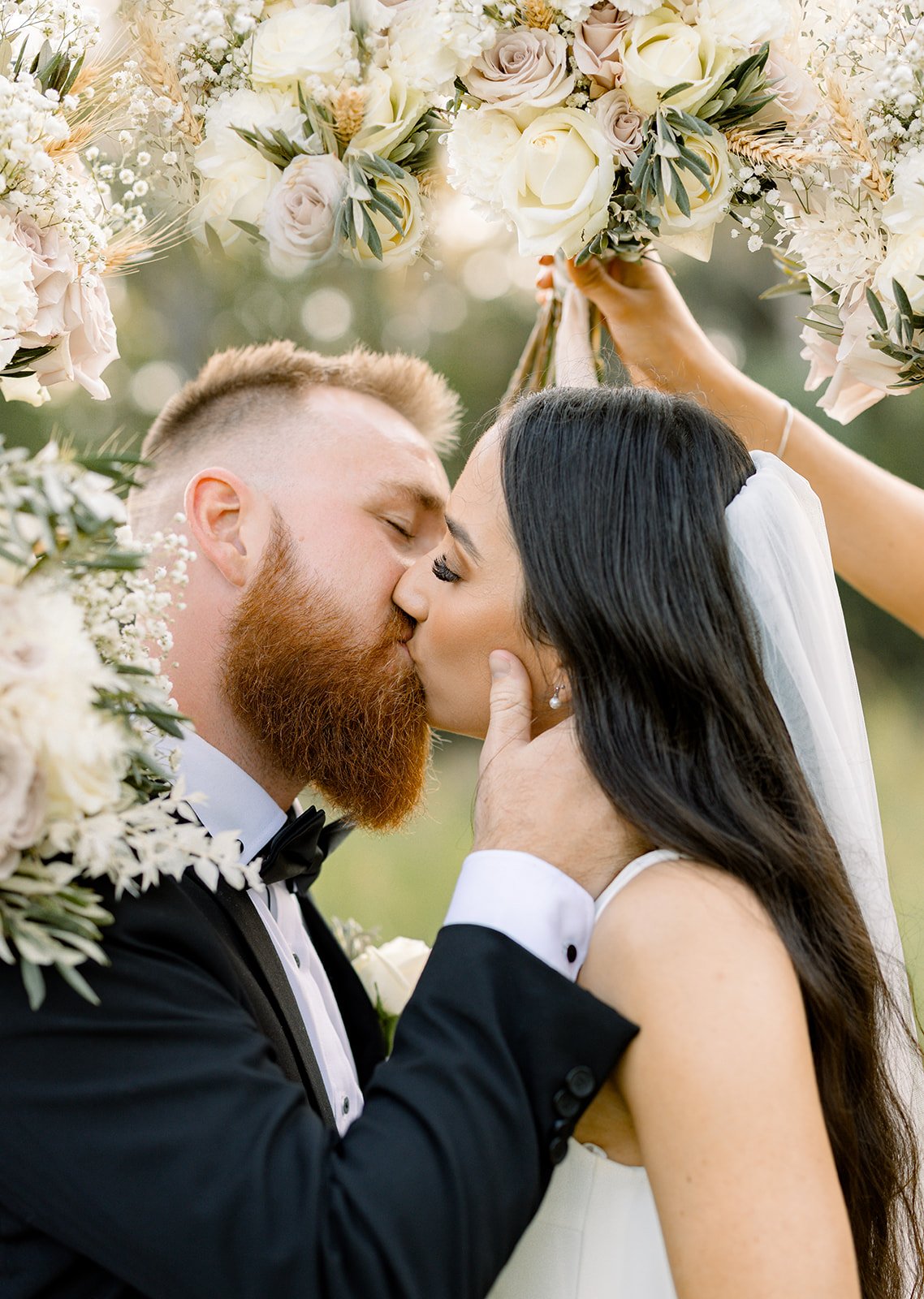 bride and groom kissing under bouquet arch