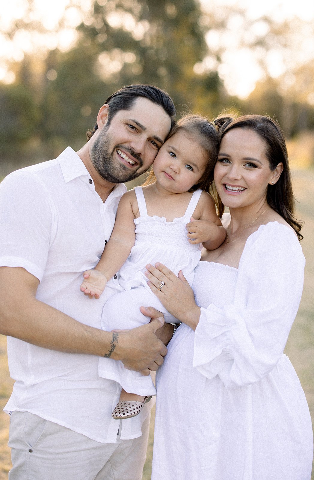 maternity session with a family of three cuddling together in a grassy field