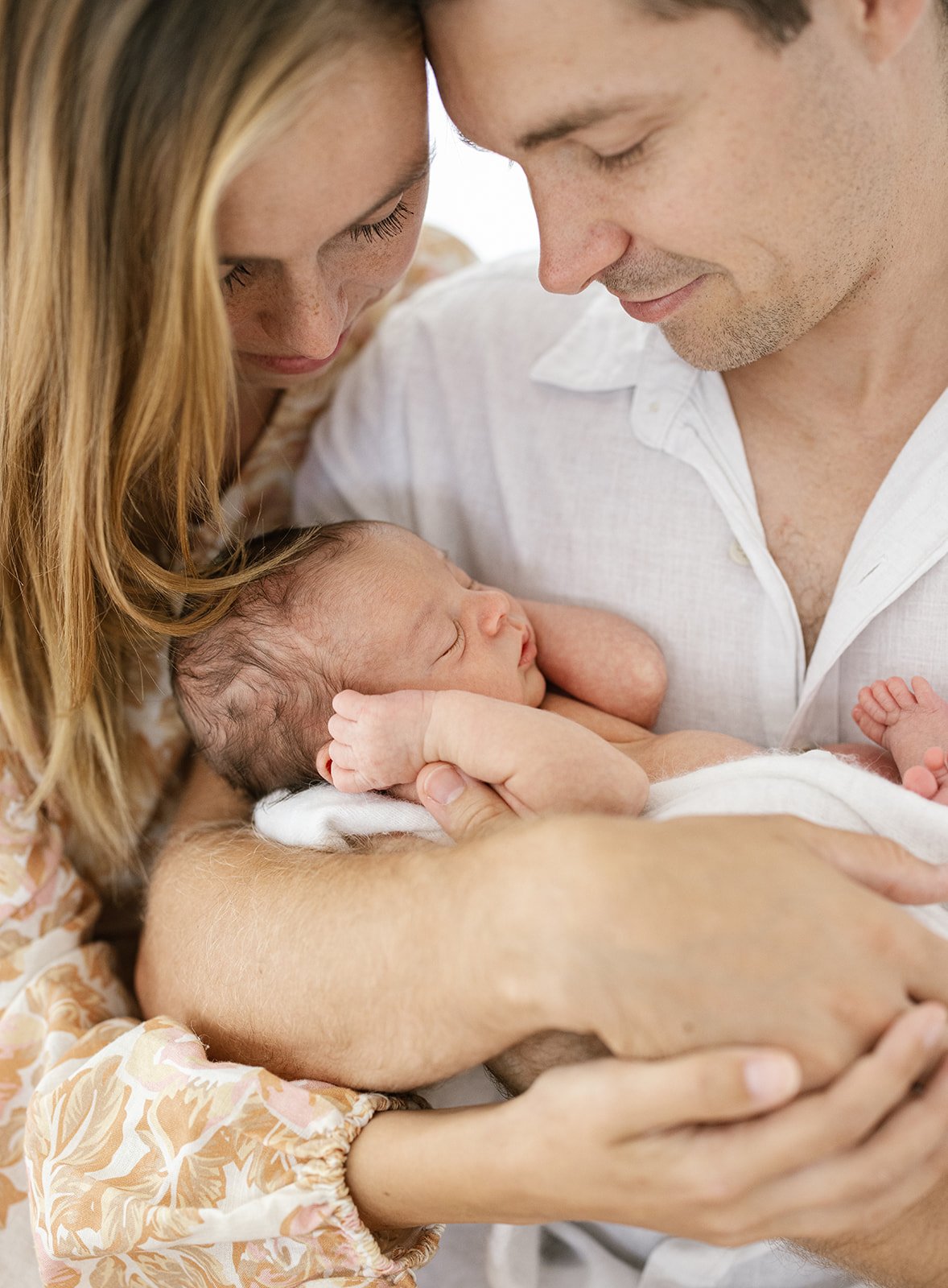 Father craddling newborn baby with her hands to her ears and mother looking over him