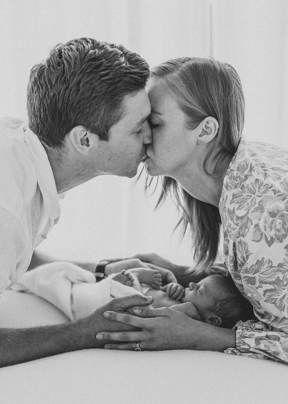 Newborn parents kissing over their sleepy baby girl