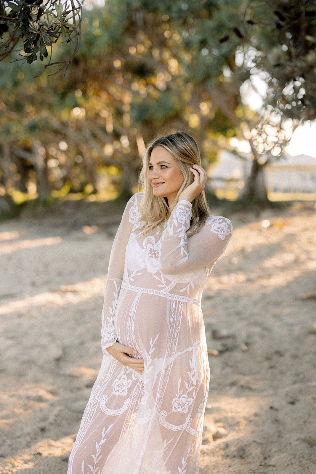 Mother-to-be holds her bump standing on a shady beach