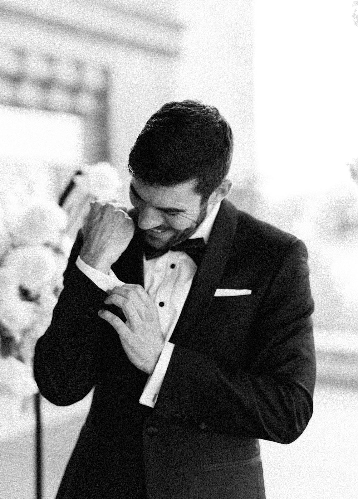 Black and white image of groom fixing cuff link