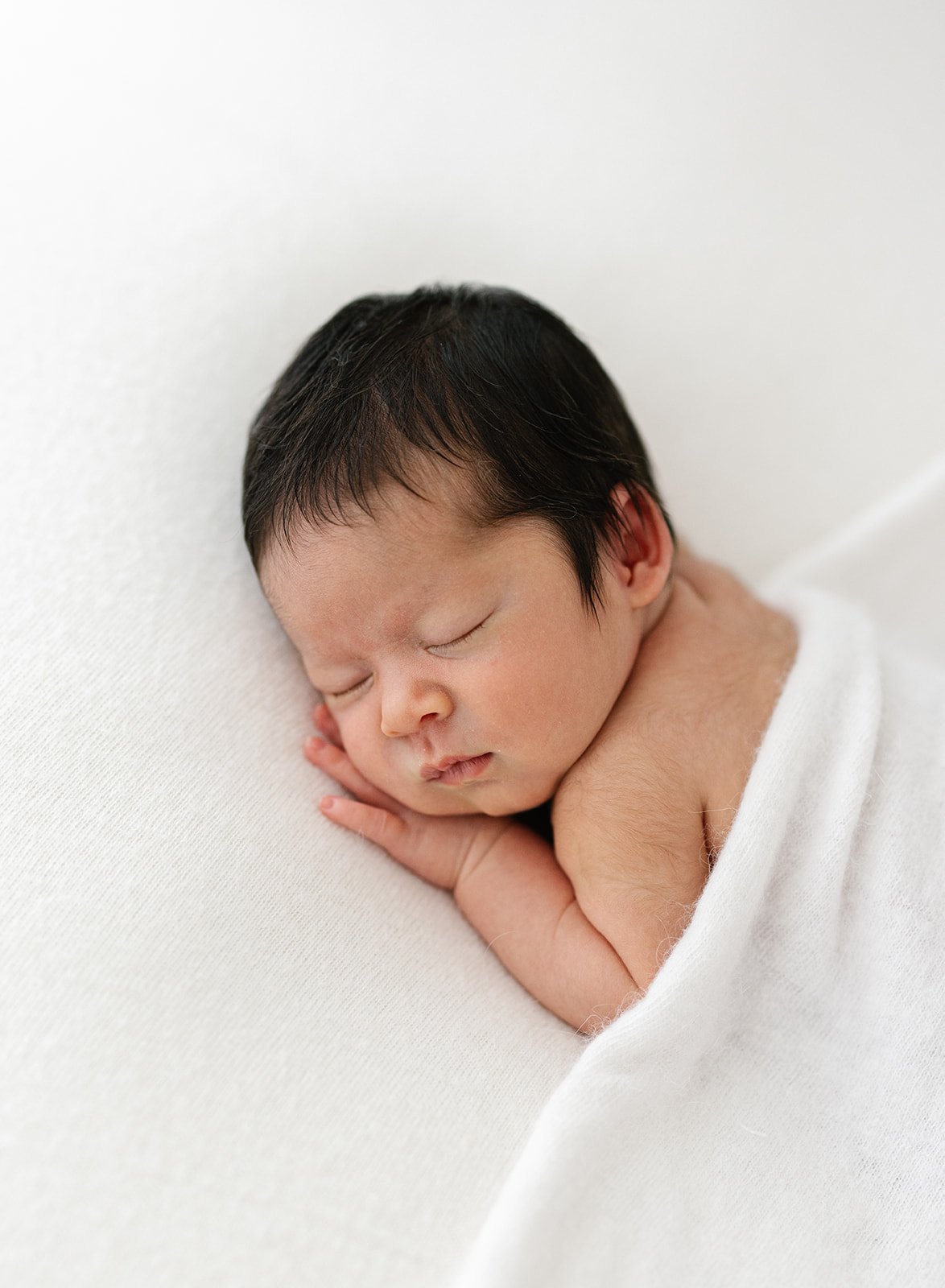 newborn baby with dark hair wrapped in white blanket
