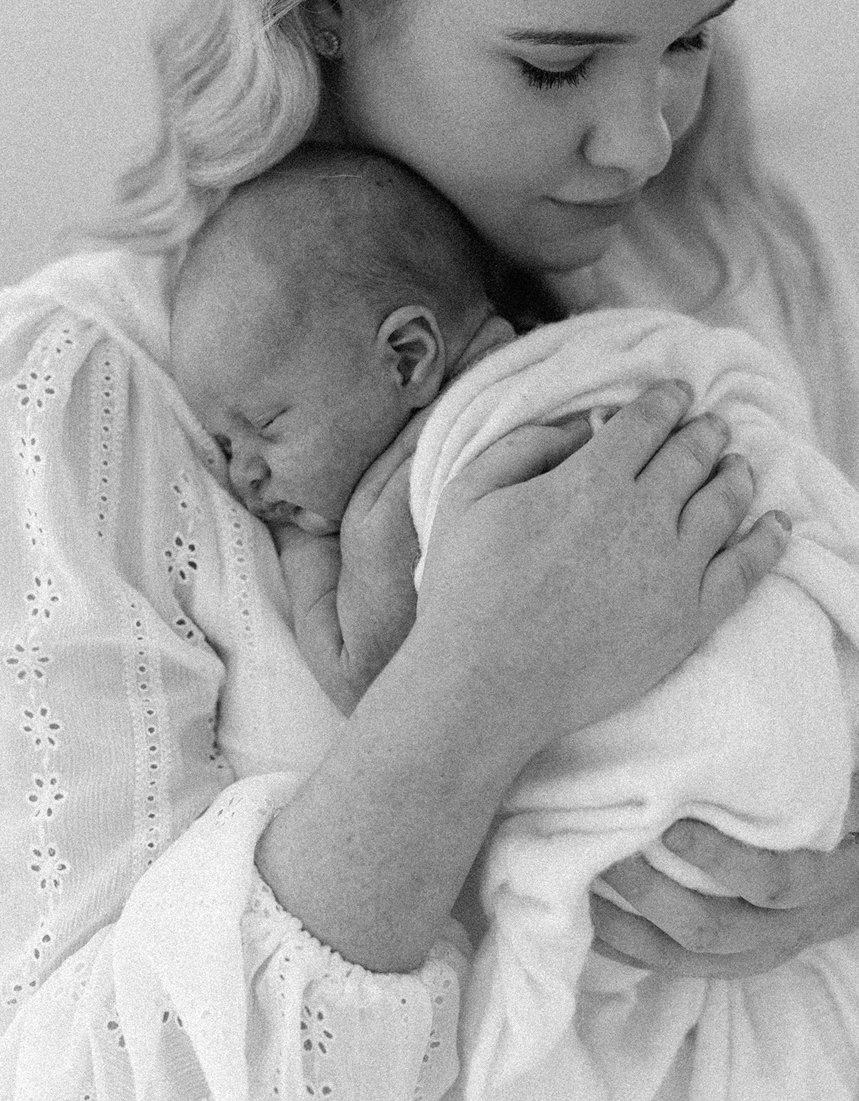 black and white photo of newborn baby cuddled into mums chest