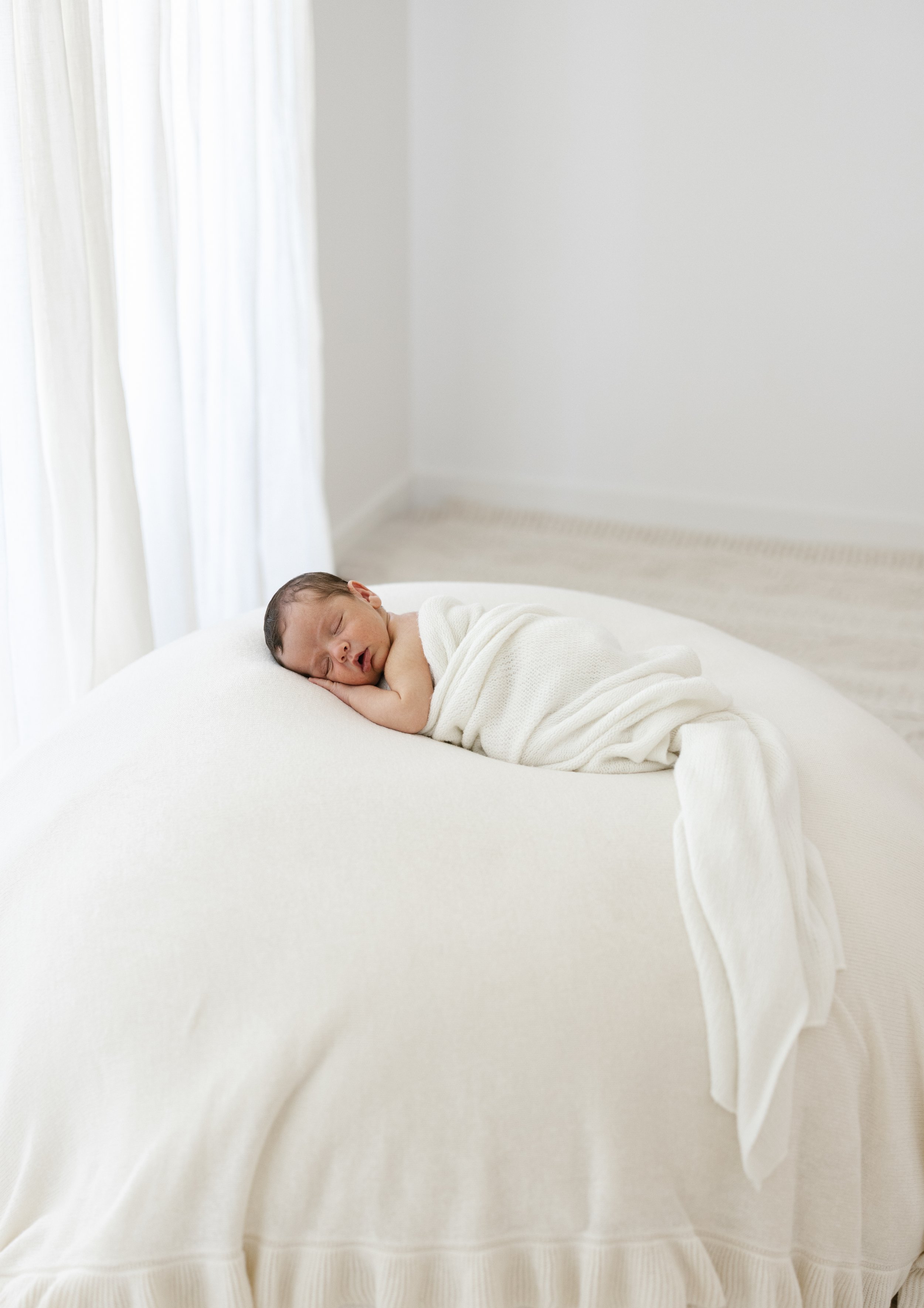 newborn baby asleep photographed on a white beanbag 