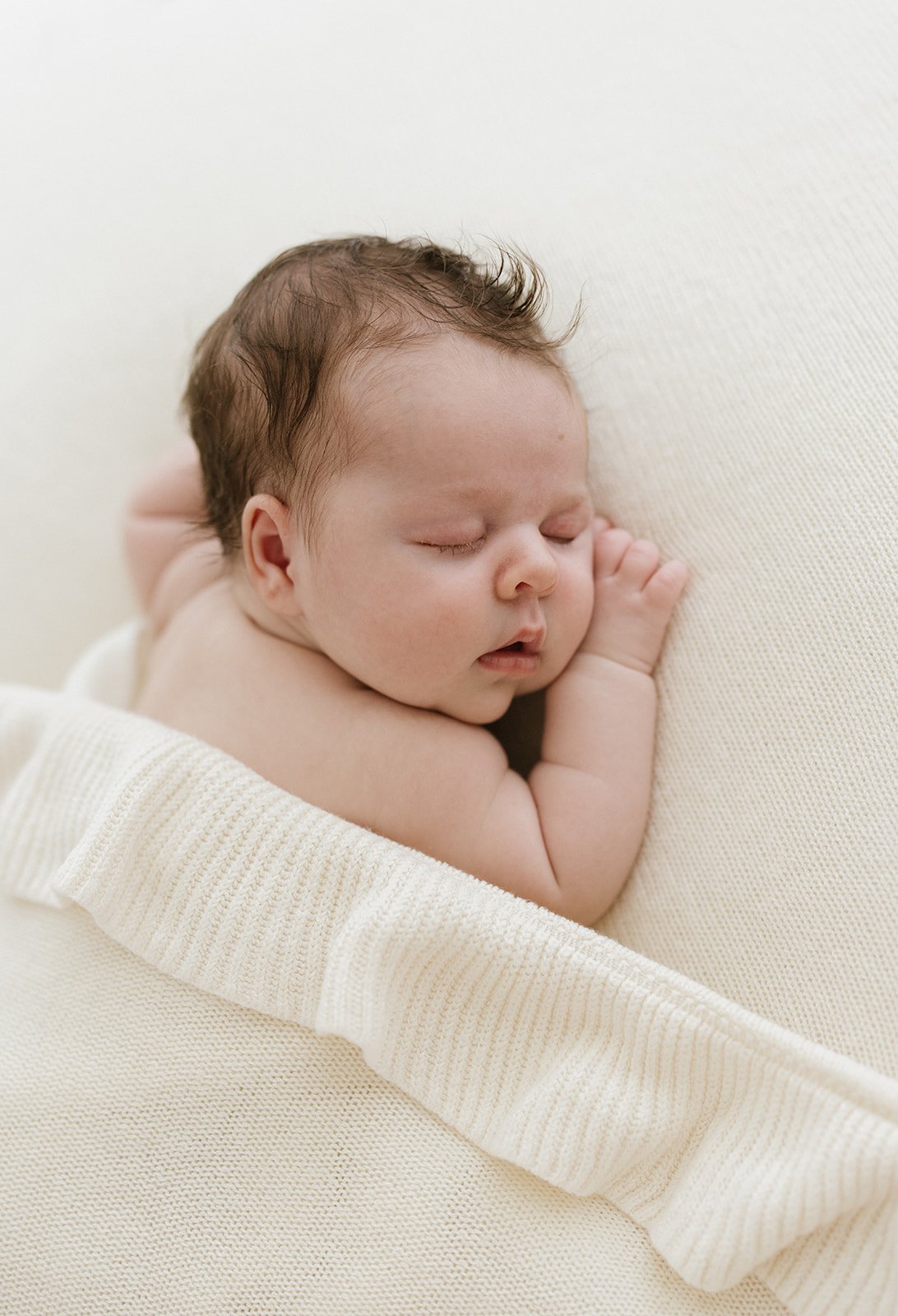 newborn baby girl laying on her belly covered by a ruffled white blanket 